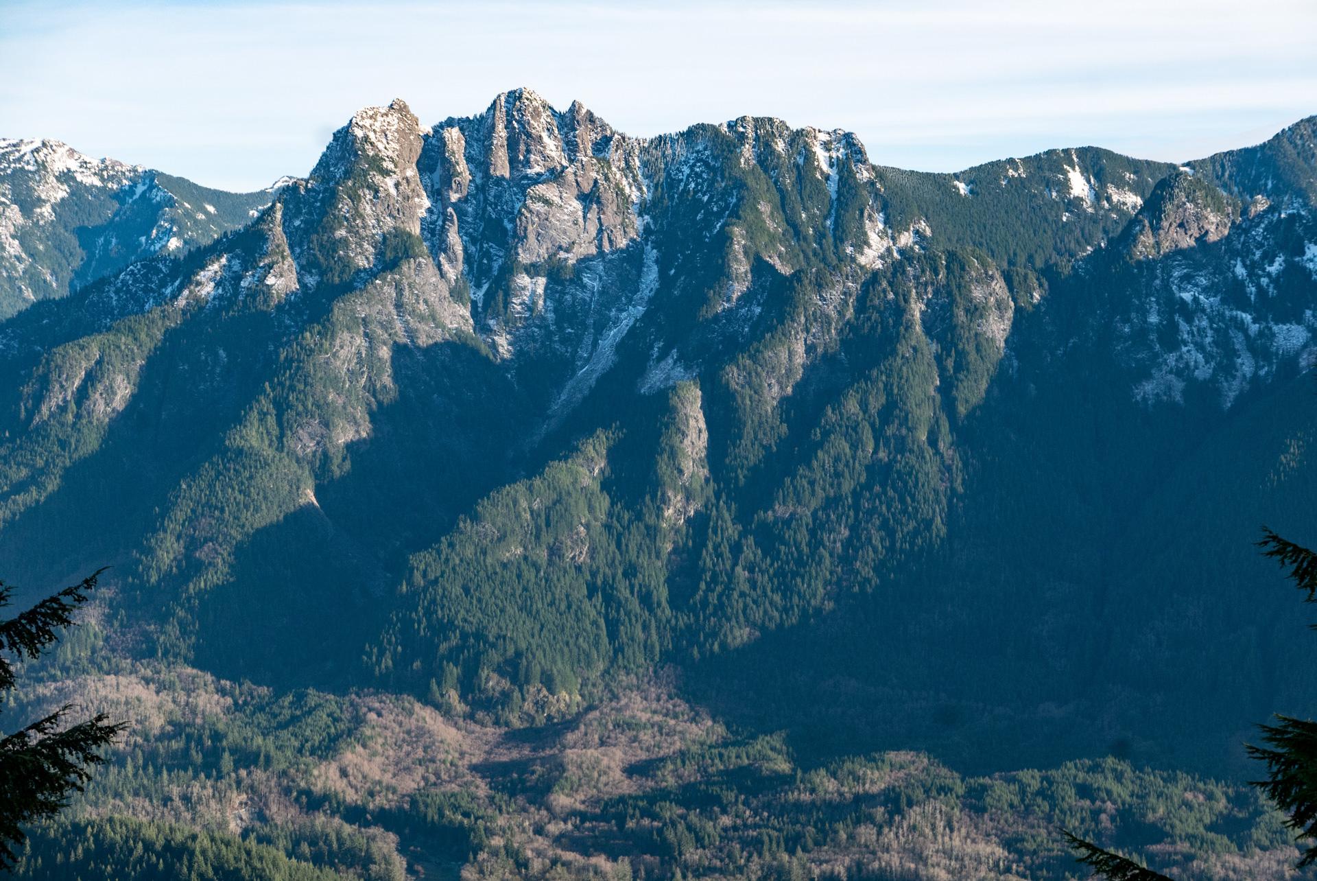 Rugged, snow-dusted mountain peaks rise above forested slopes under a clear sky.