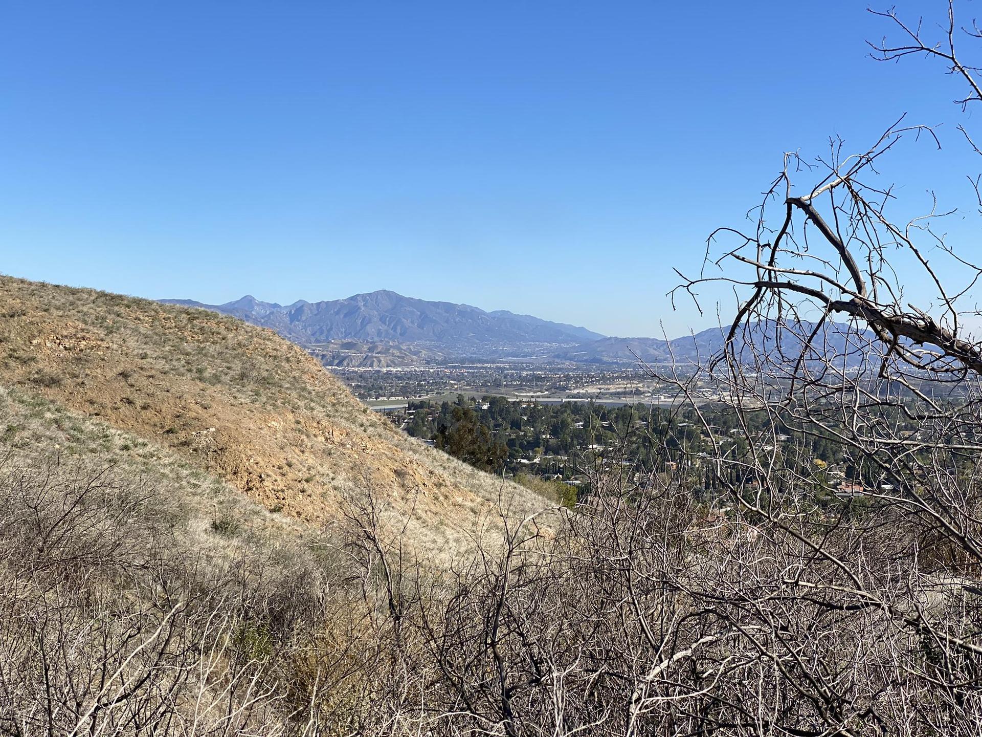 Sunny view of a dry hillside overlooking a valley and distant mountains.