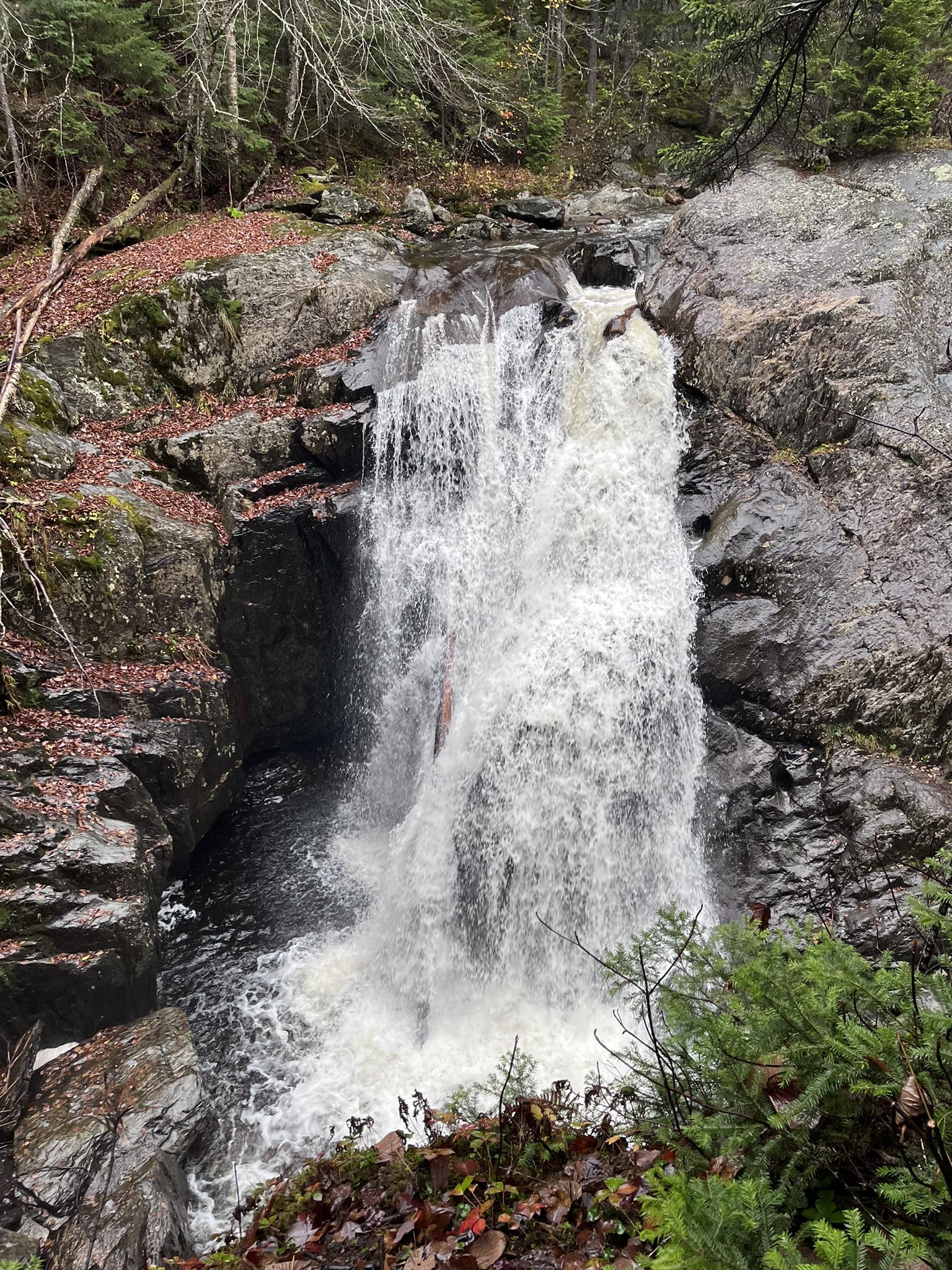 A kayaker descends a powerful waterfall surrounded by autumn forest and dark rocks.