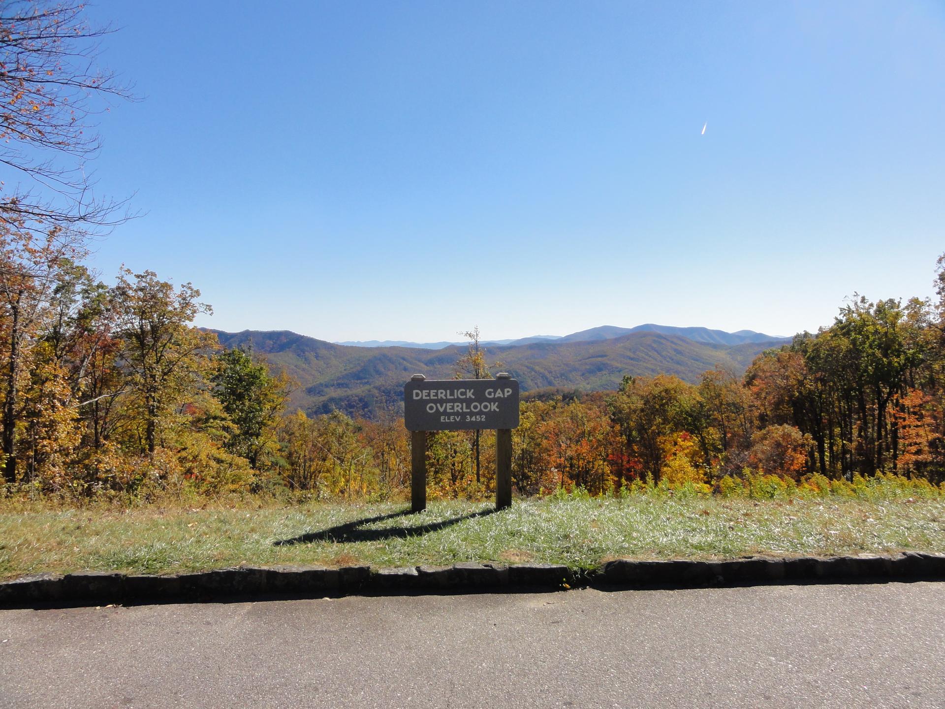 Wooden sign overlooks a vast autumn mountain range under a clear blue sky.