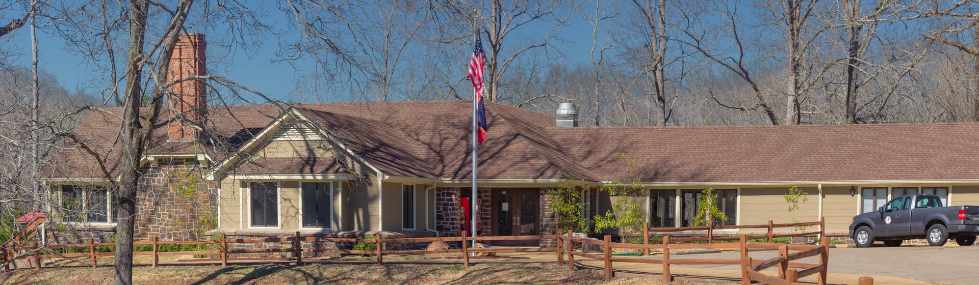 A long building with a flag, bare trees, and a parked truck on a bright day.