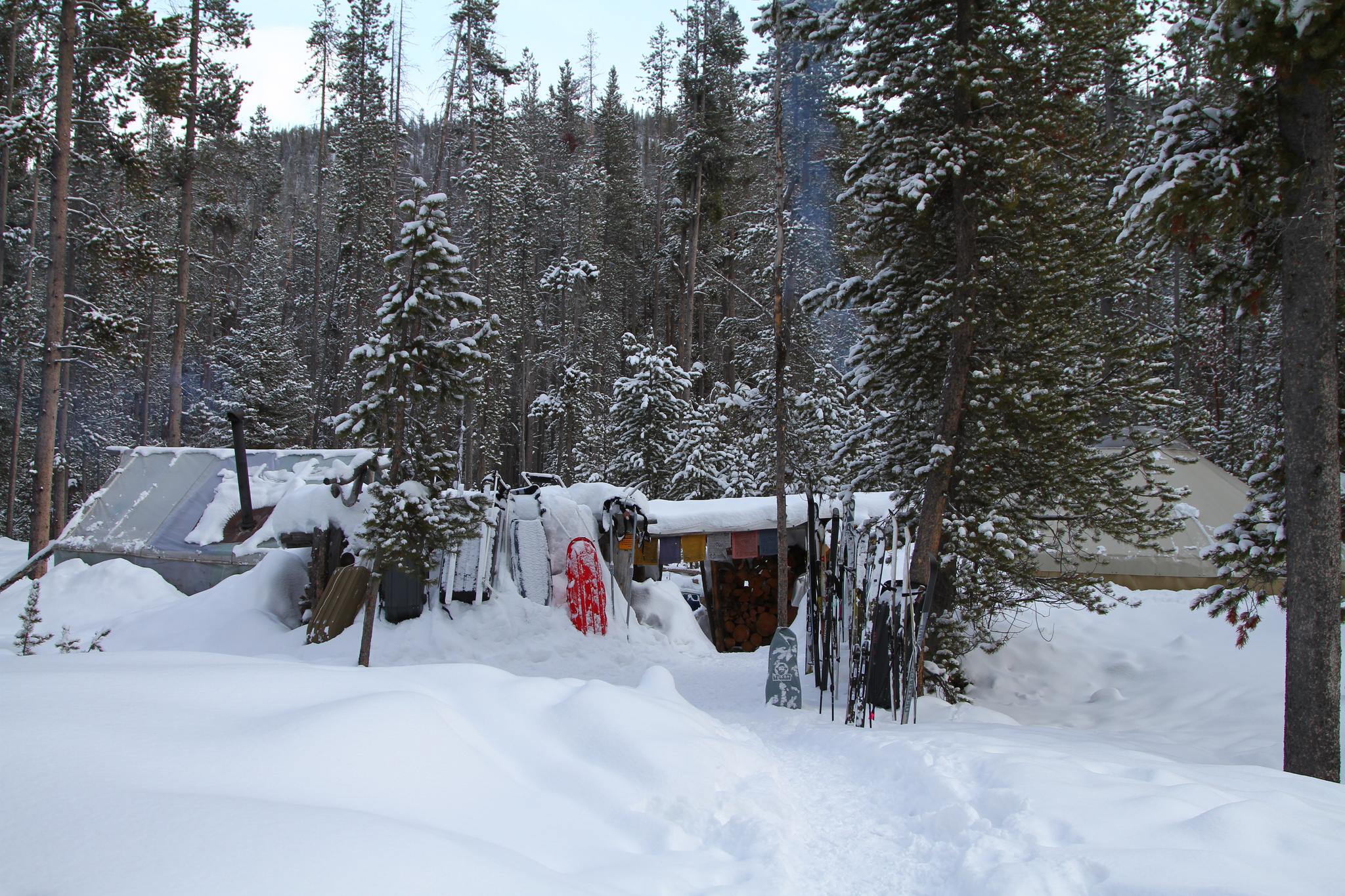 Snow-covered rustic cabin in a dense winter forest with skis.