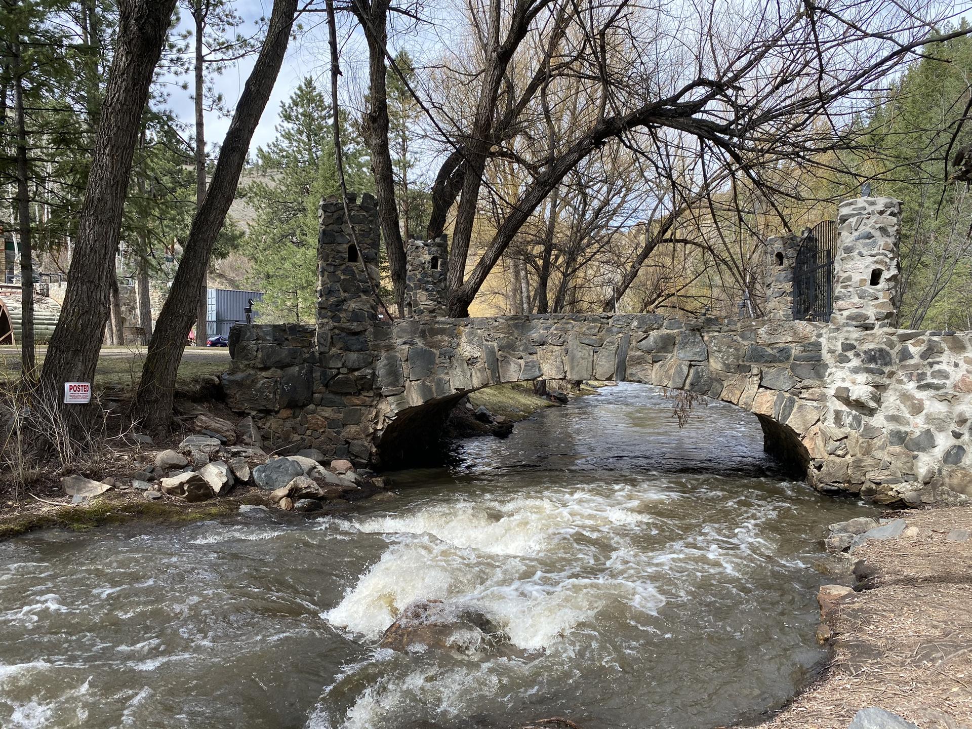 Stone bridge with arches over a rushing river, surrounded by trees.
