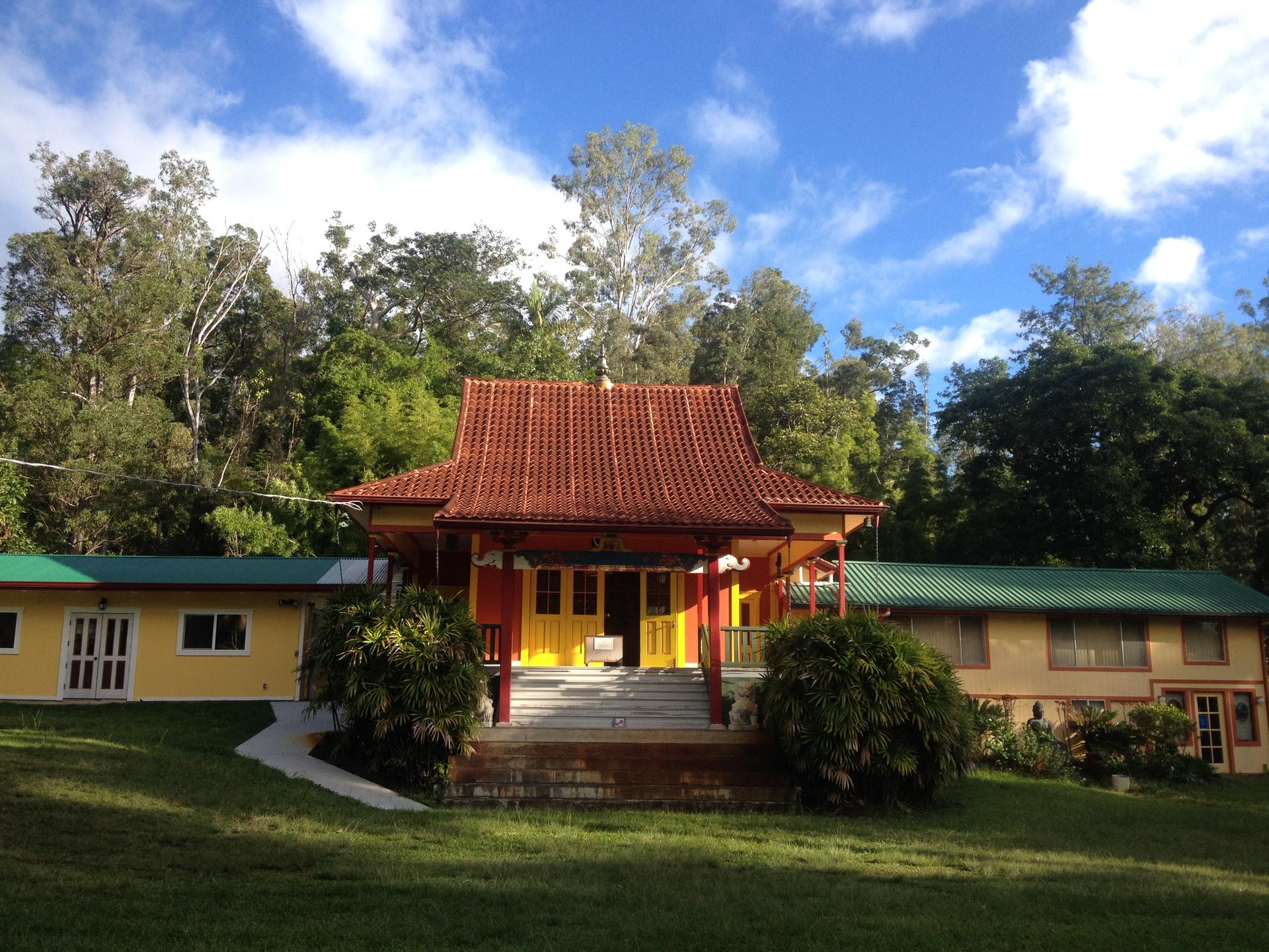 Traditional red-roofed building nestled among green trees under a bright blue sky.