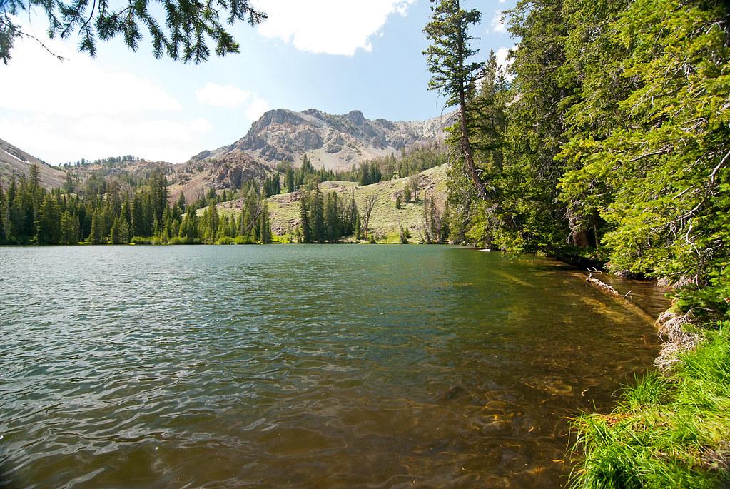 A serene mountain lake surrounded by forests and rocky peaks under bright daylight.