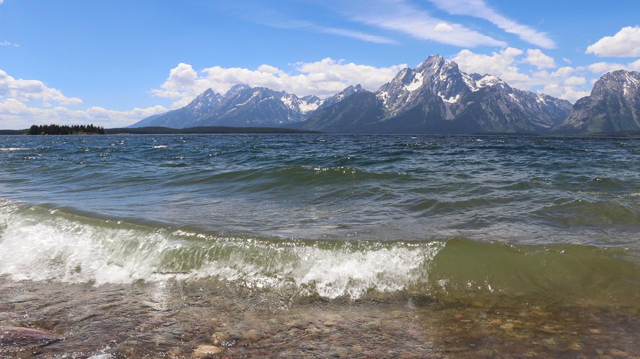 Choppy lake water with snow-capped mountains under a bright blue sky.
