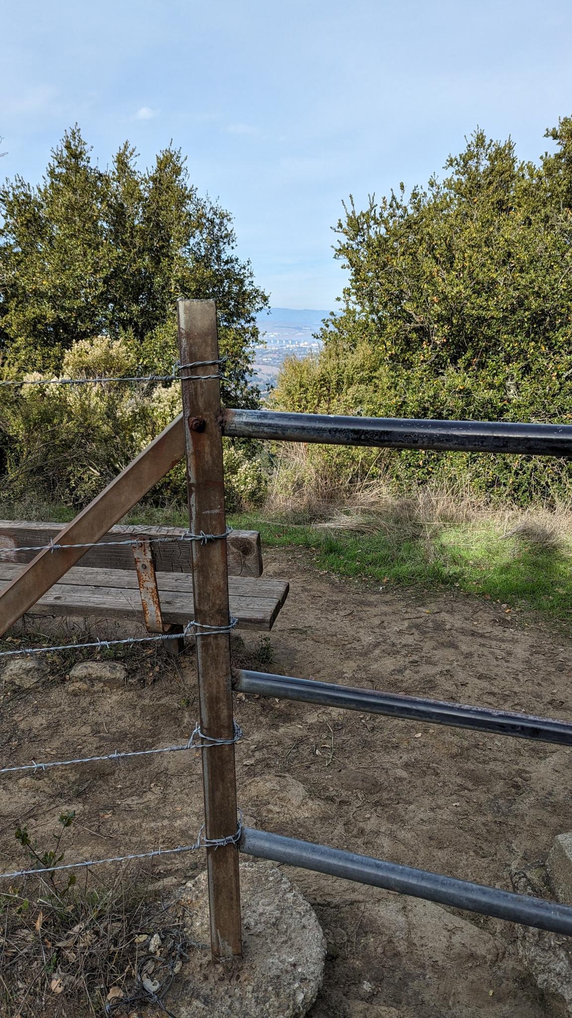 Wooden fence post with wire in a wooded area, distant view beyond.