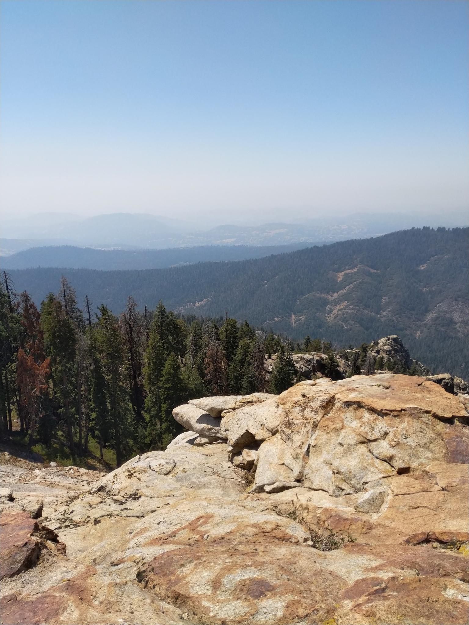 Rocky mountain overlook with a dense forest and hazy distant peaks. - Big Baldy Ridge Trail