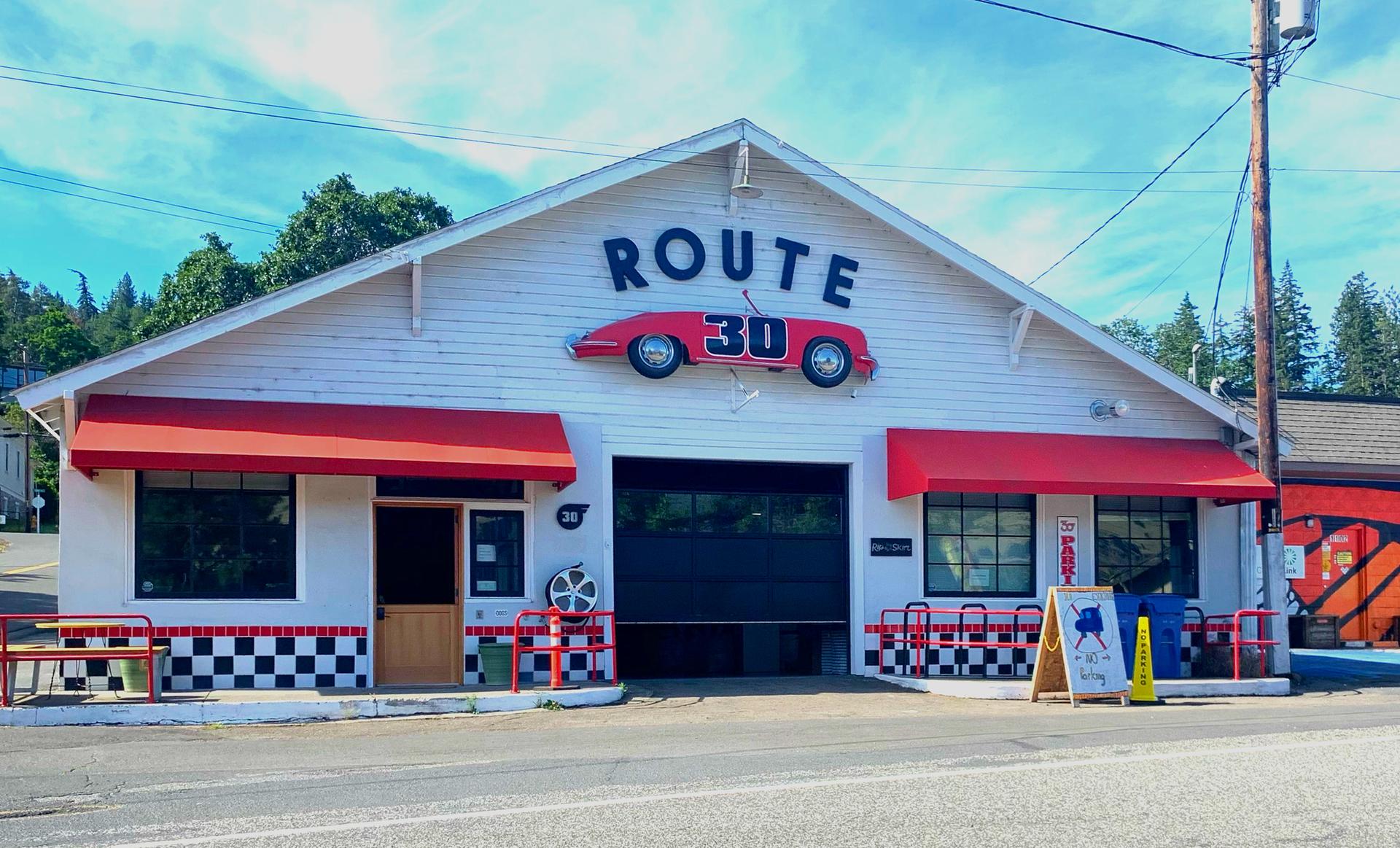 A white building with 'ROUTE 30' sign and red awnings under blue sky.