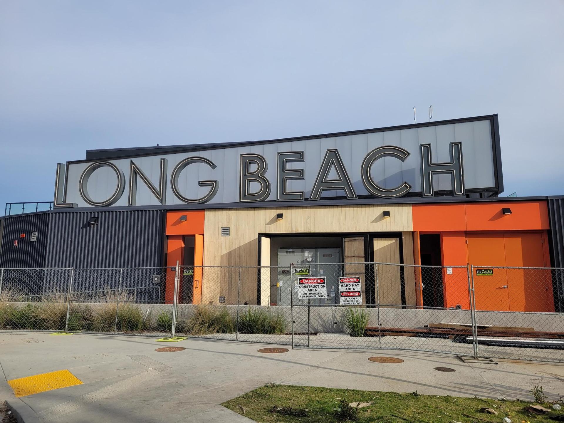 A modern building with a large sign, surrounded by a fence, under clear skies.