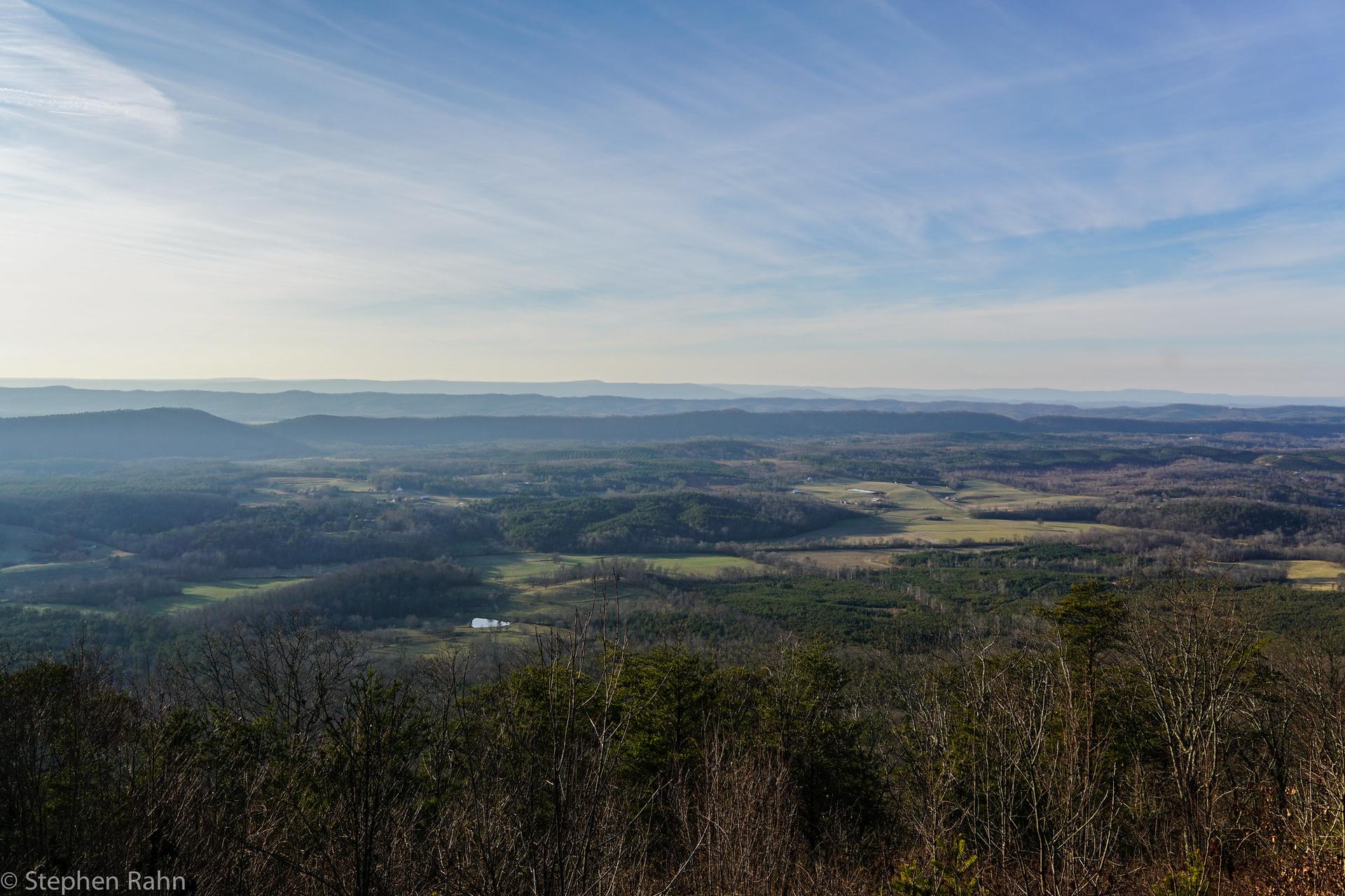 Wide panoramic view of a hazy, forested valley under a clear sky.