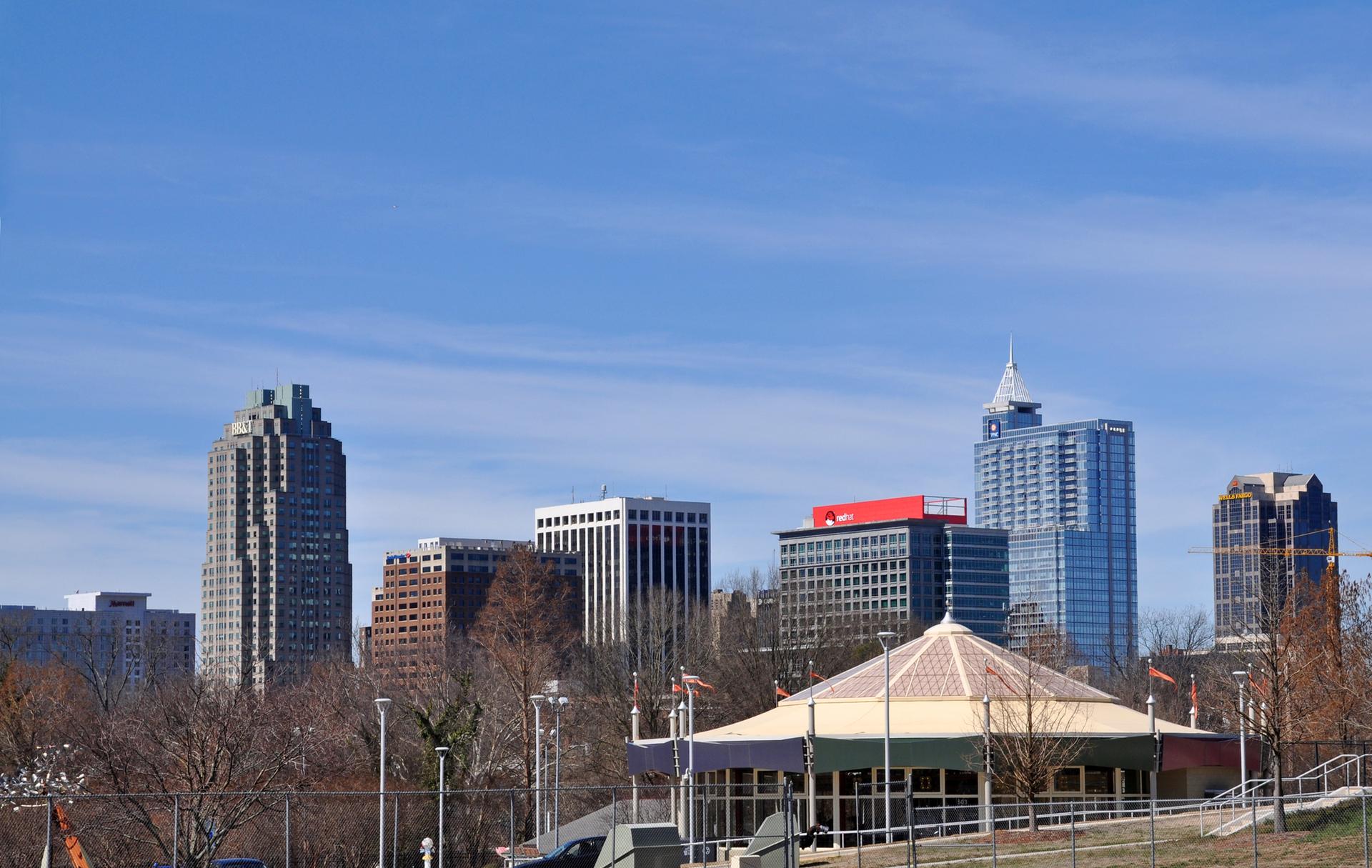 A city skyline with tall buildings behind a colorful carousel under blue sky.