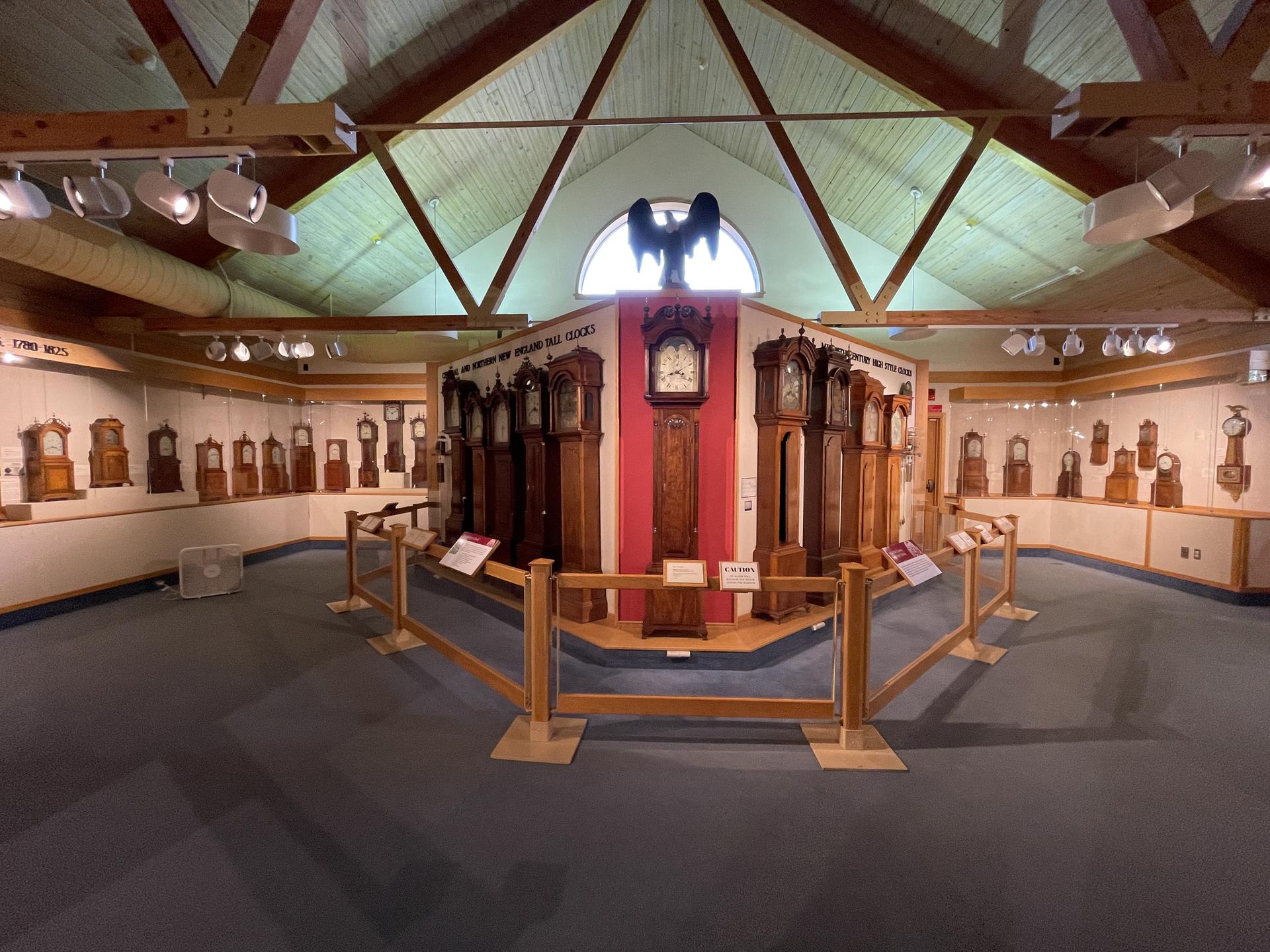 A large room displaying numerous grandfather clocks under bright indoor lighting.