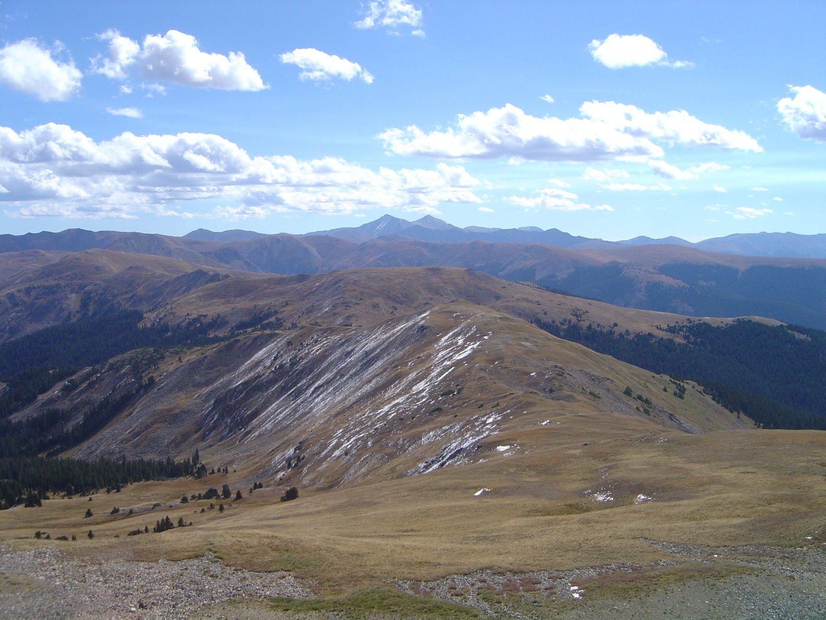 Expansive mountain landscape with patches of snow under a bright sky.