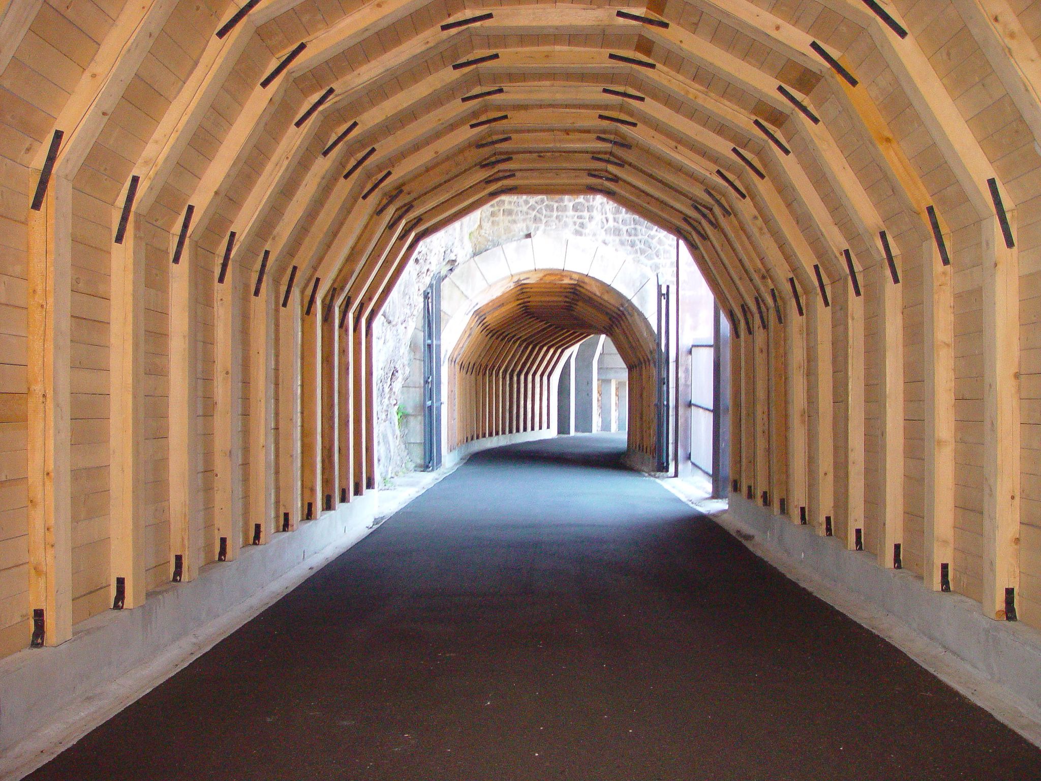 A long, light-wood tunnel with a paved path leading to a brighter stone archway. - Historic Columbia River Highway and Memaloose Hills Loop