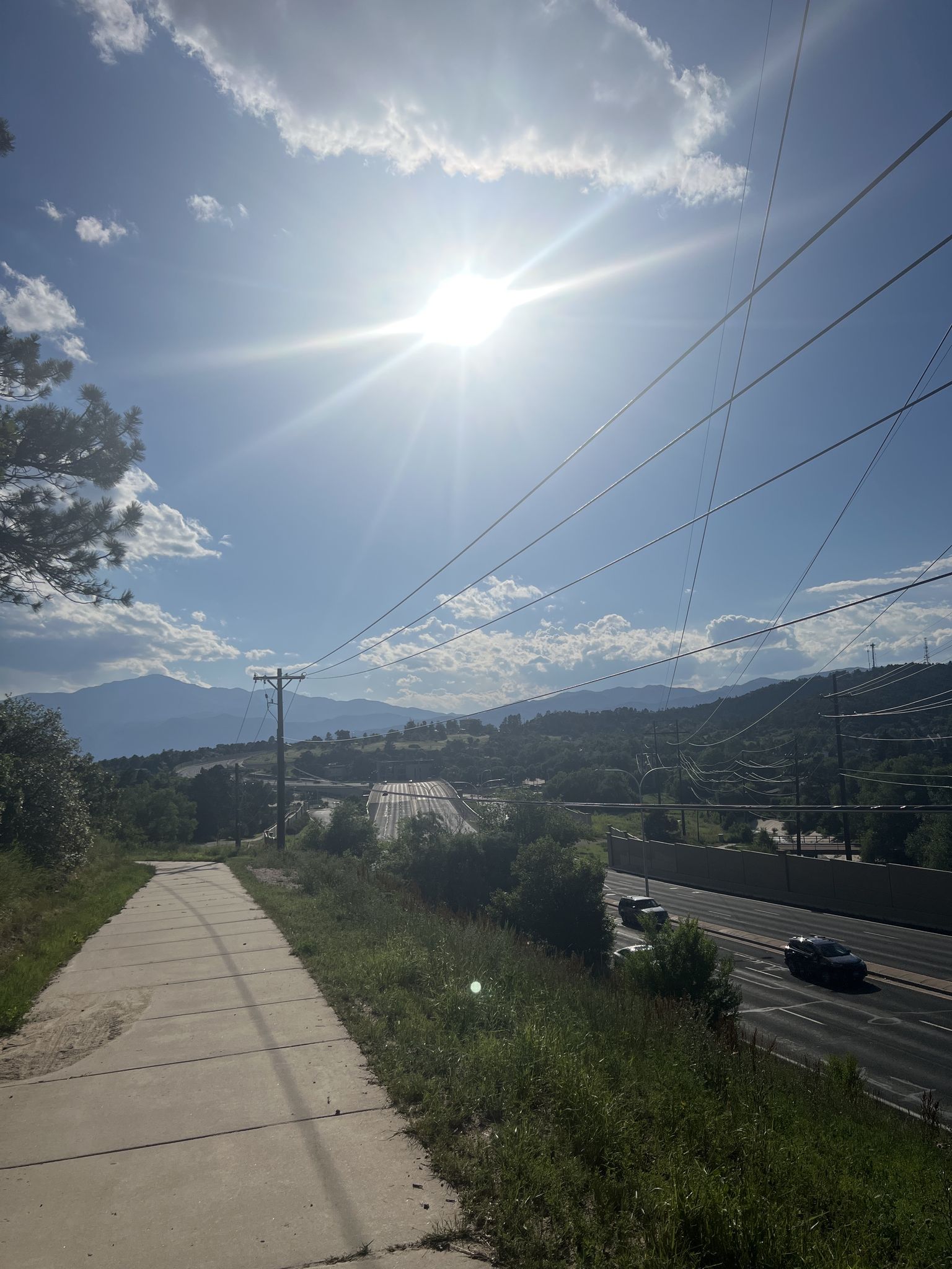 Bright sun shines over a highway with distant mountains and power lines. - Austin Bluffs Trail – Palmer Park Scenic View loop from Switchbacks Training Stadium