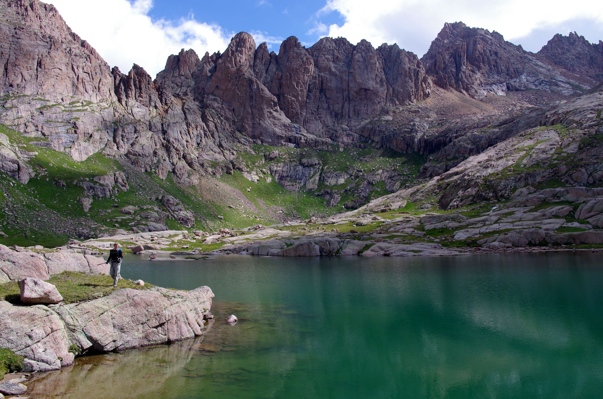 Person stands on rocks beside a clear mountain lake with rugged peaks. - Needle Creek Trail to Chicago Basin