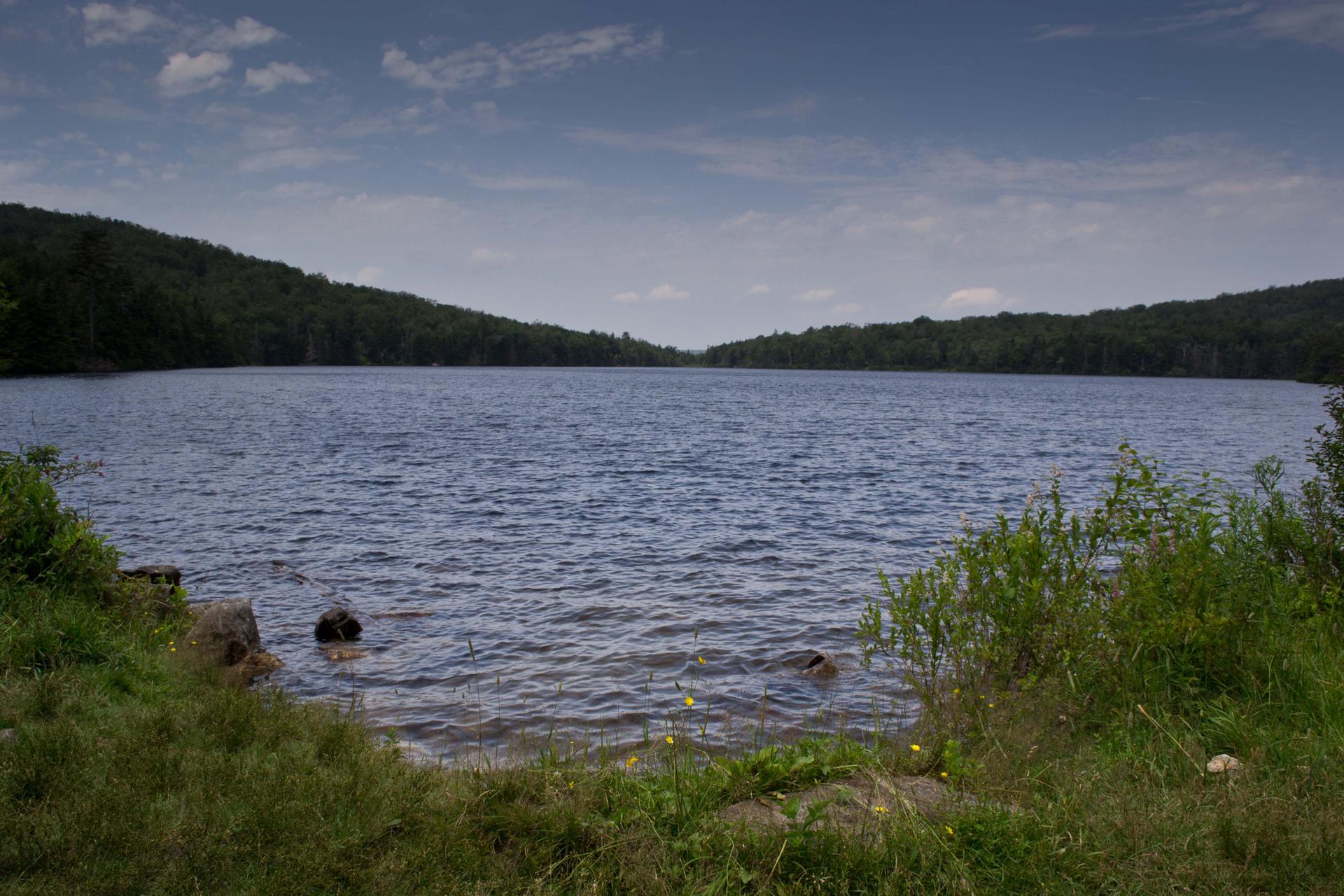 Dark lake water with forested hills under a partly cloudy sky.
