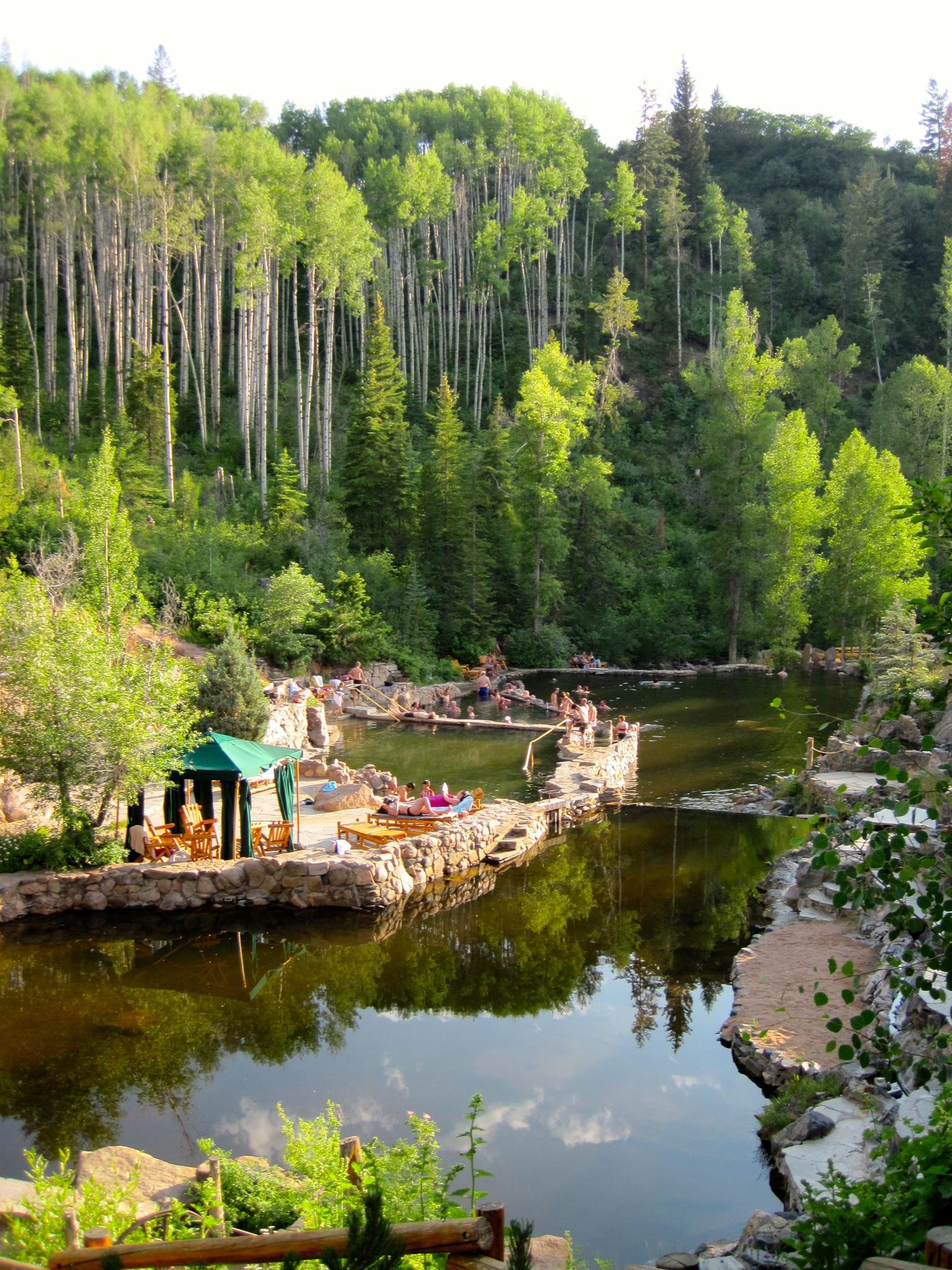 People relax in natural pools surrounded by lush green forest under bright daylight.