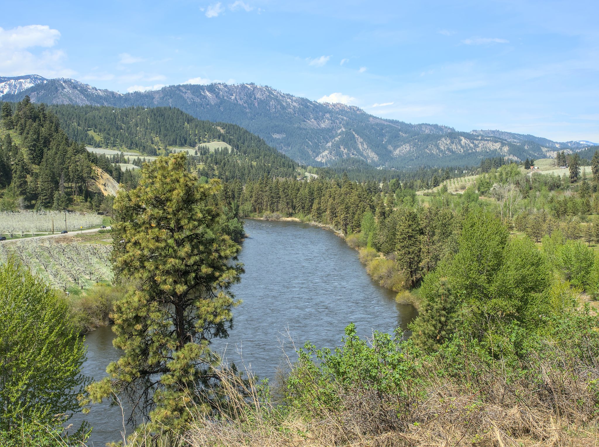 River flowing through a green valley with dense forests and snow-capped mountains. - Leavenworth to Peshastin Pinnacles State Park