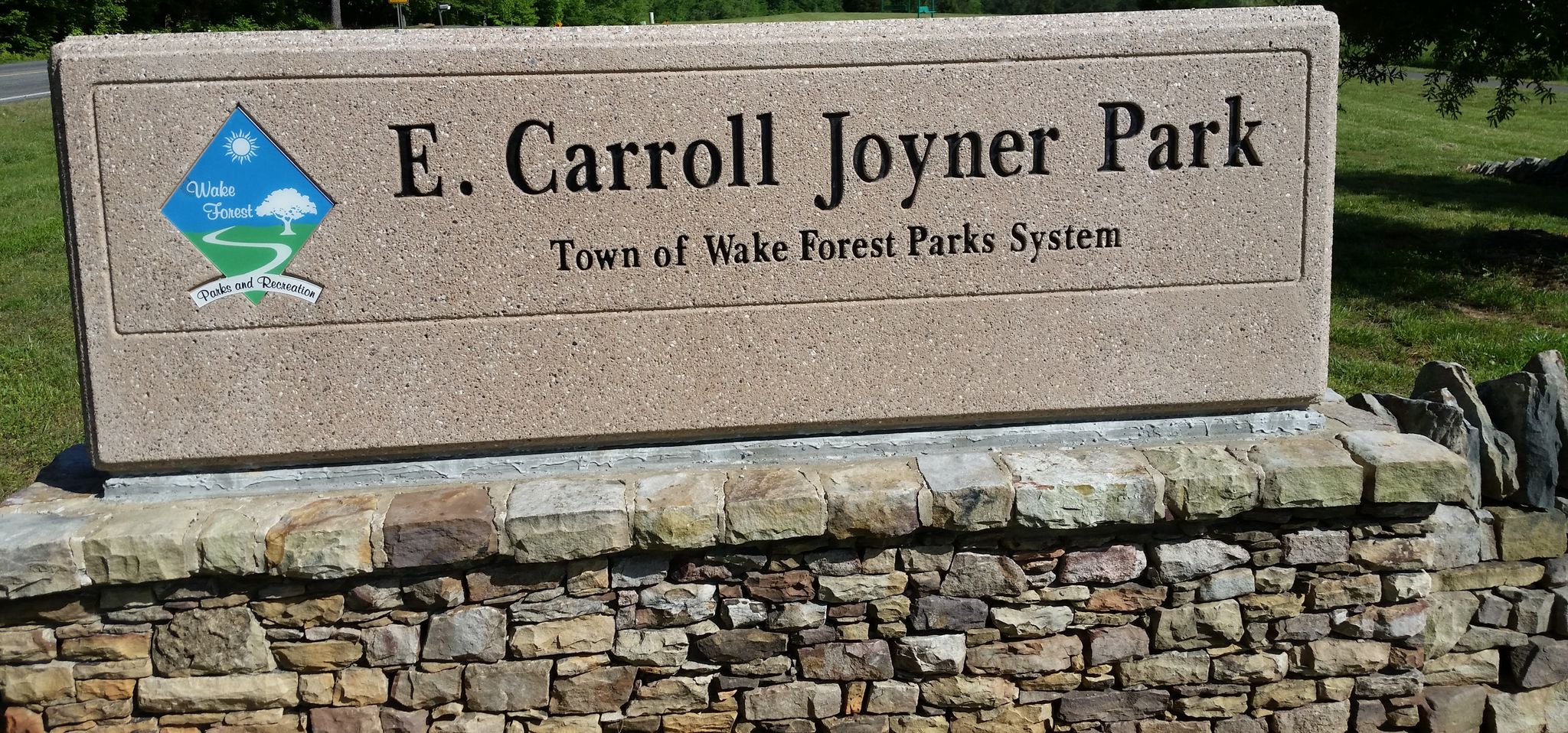 A large stone sign on a rock wall with green grass under bright daylight. - E. Carroll Joyner Park from Sleepy Hollow loop