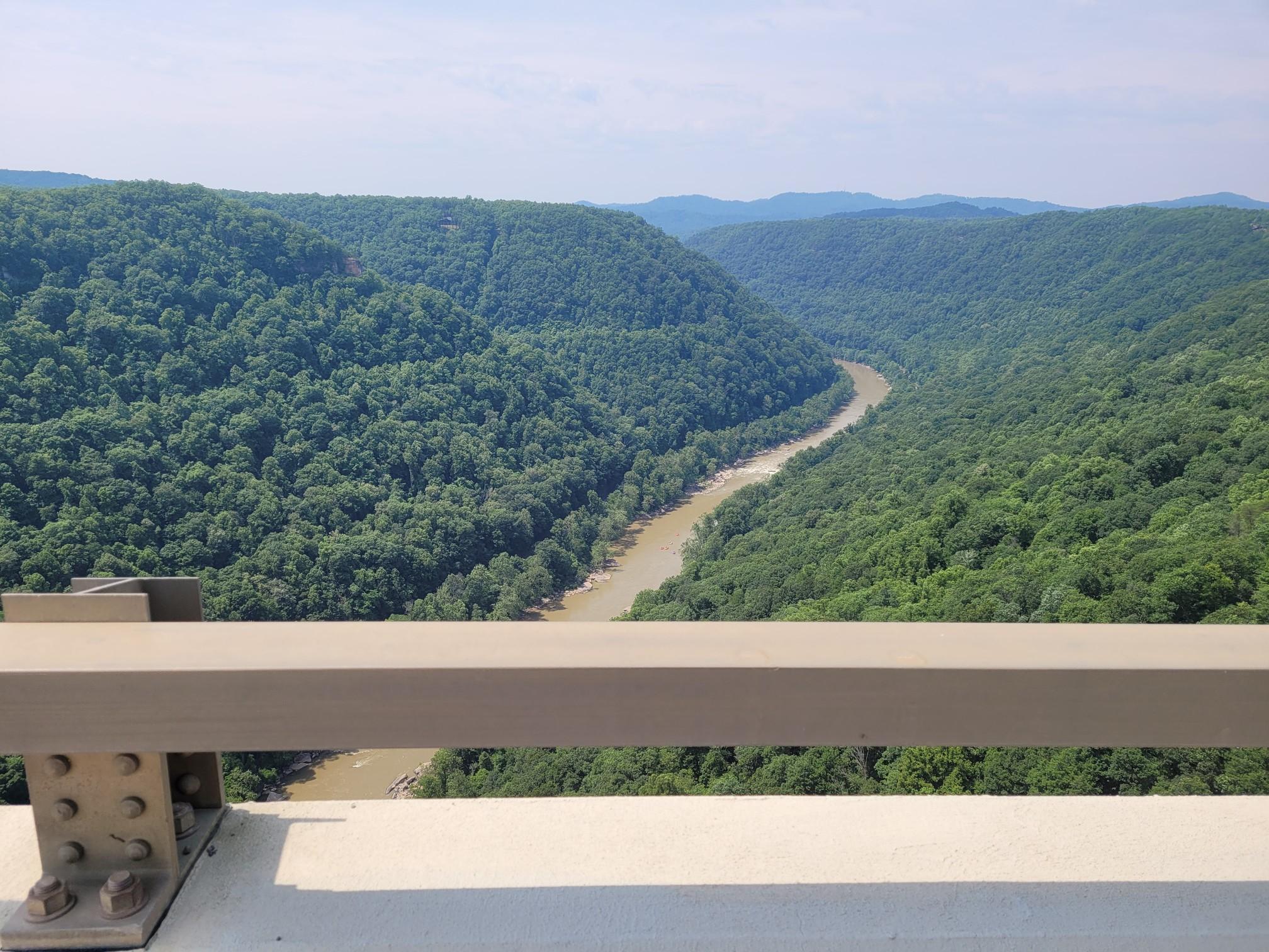 A wide, brown river winds through a vast green forested valley from a bridge.