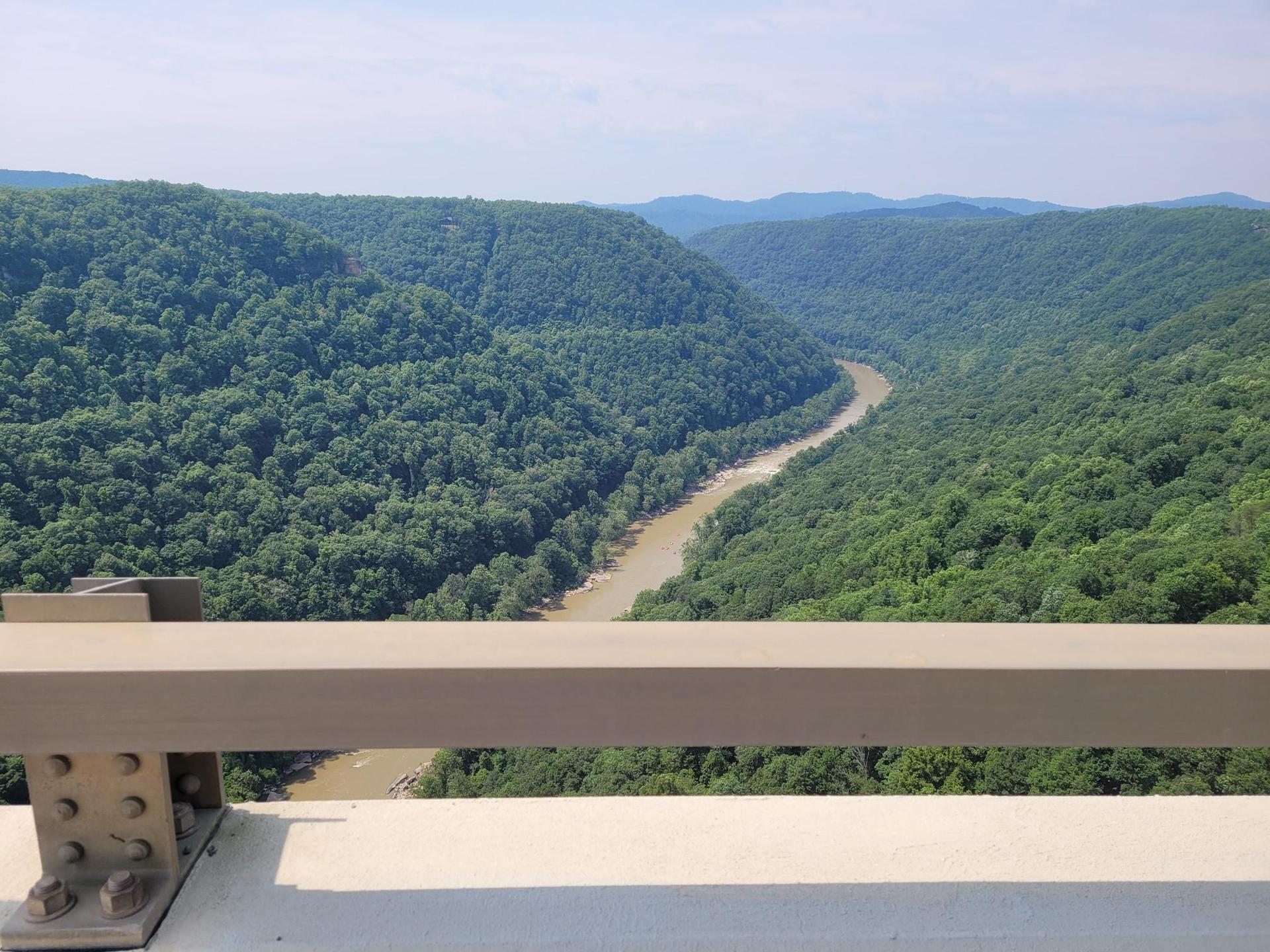 A wide, brown river winds through a vast green forested valley from a bridge.