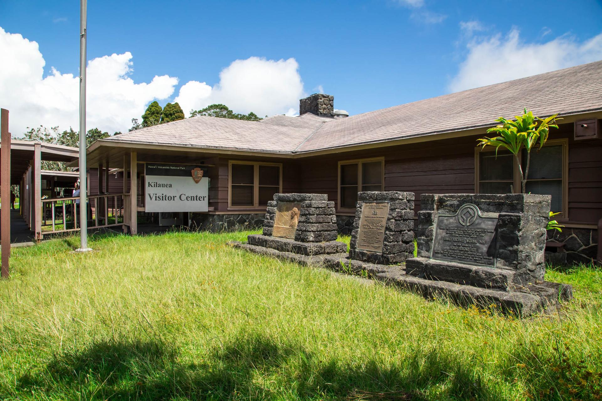 A visitor center building with a sign, stone monuments, and green grass.