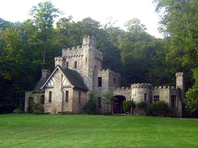 Stone castle with turrets and green roof, surrounded by lush forest.