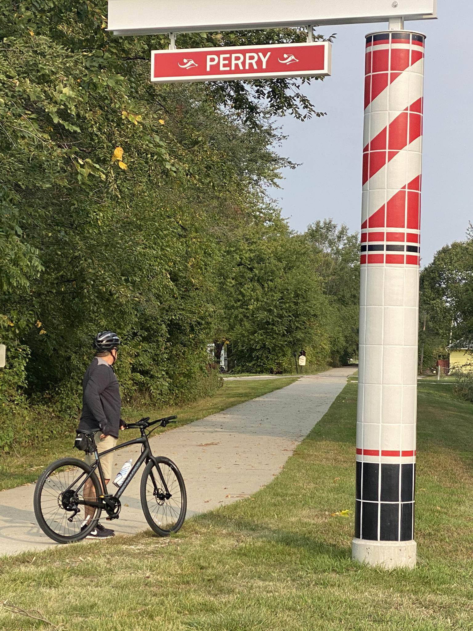 A person with a bicycle stands next to a striped pole and red sign.
