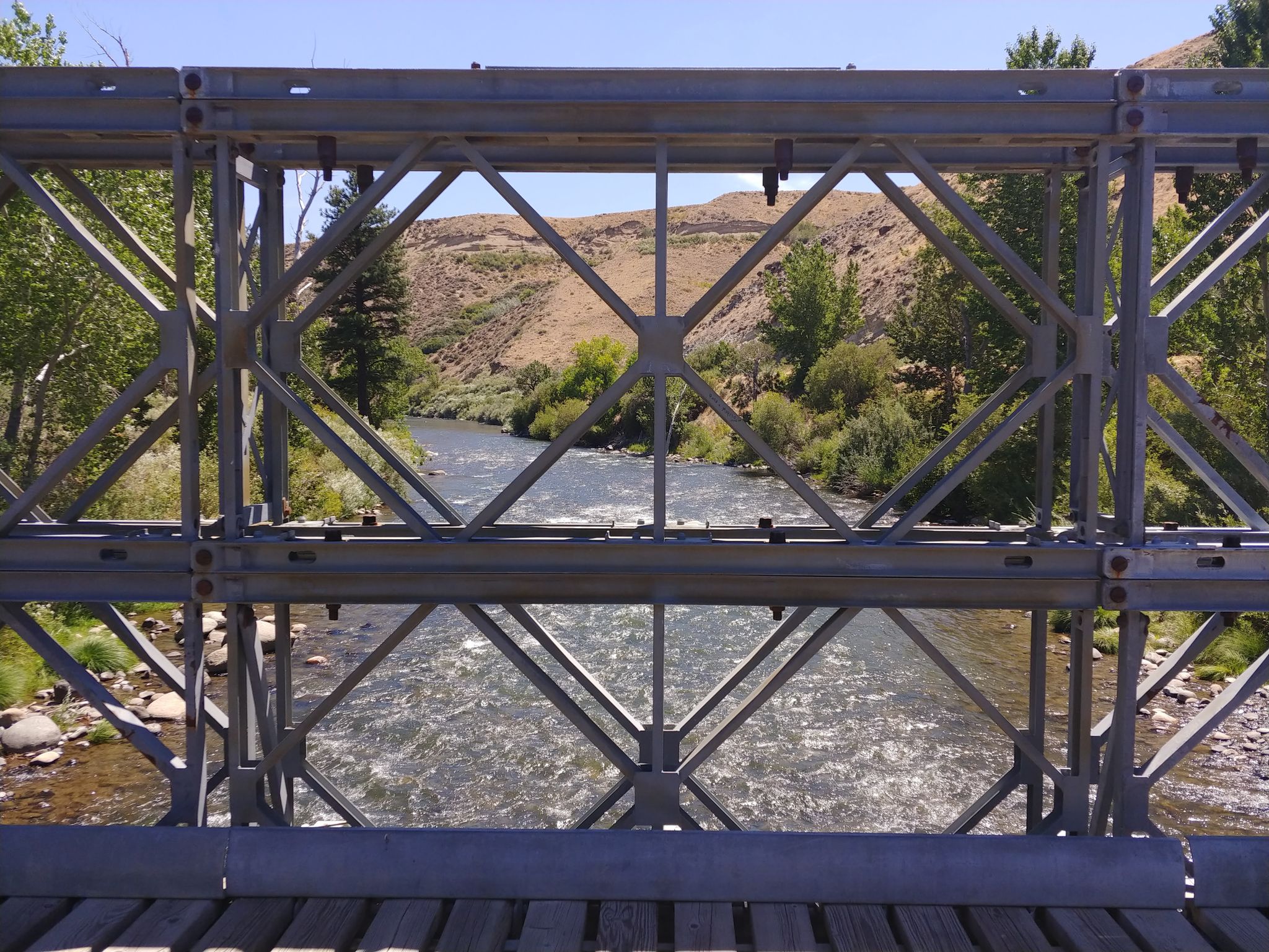 View through a metal bridge structure of a river and distant hills. - Tom Cooke and Steamboat Ditch Loop