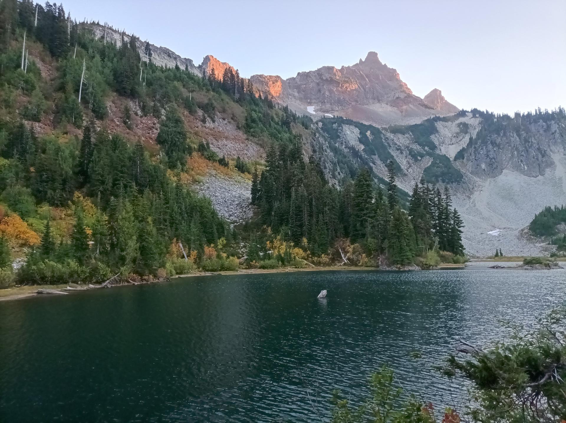 Mountain lake reflecting a rocky, forested peak with autumn colors in warm light.