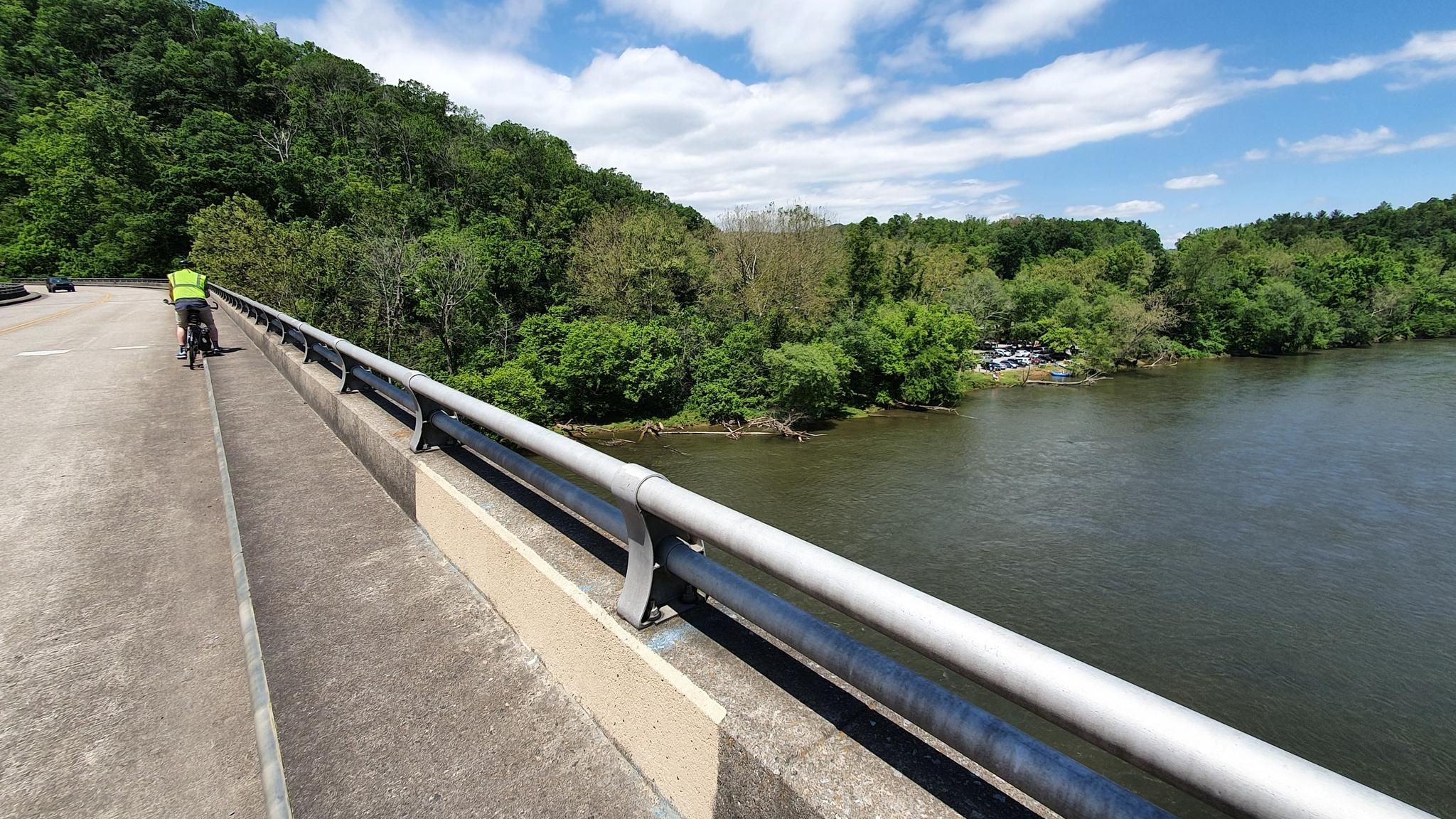 A cyclist rides on a bridge overlooking a wide river and forest. - Mountains-to-Sea Trail