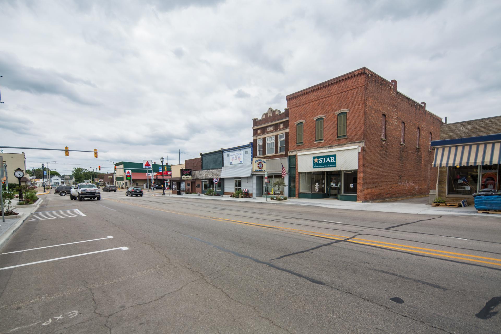 A street with brick buildings and cars under an overcast sky.