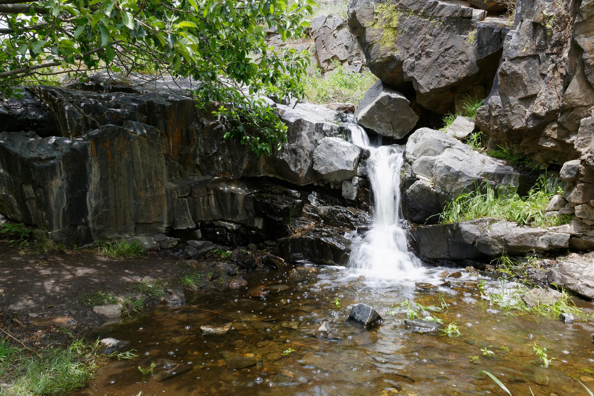 A small waterfall cascades over dark rocks into a shallow pool.