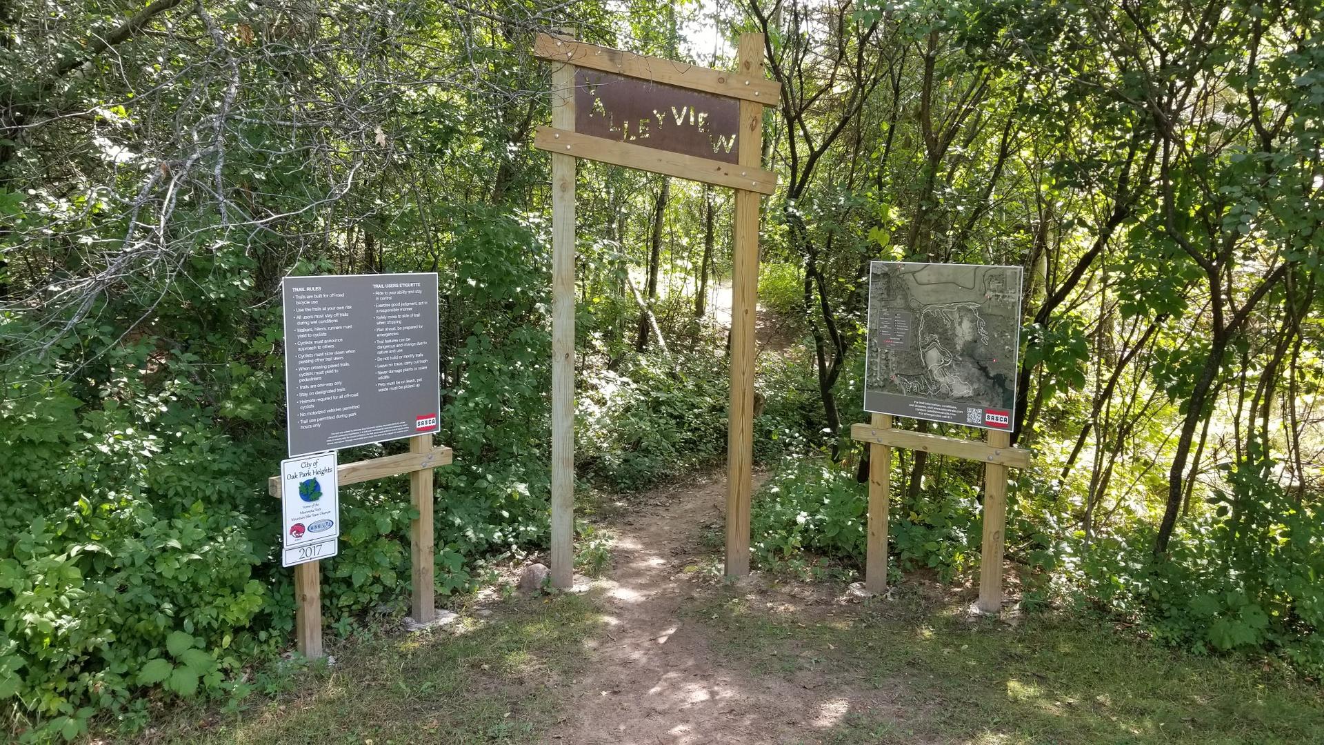 Sunny dirt path entrance with a wooden archway and information signs.