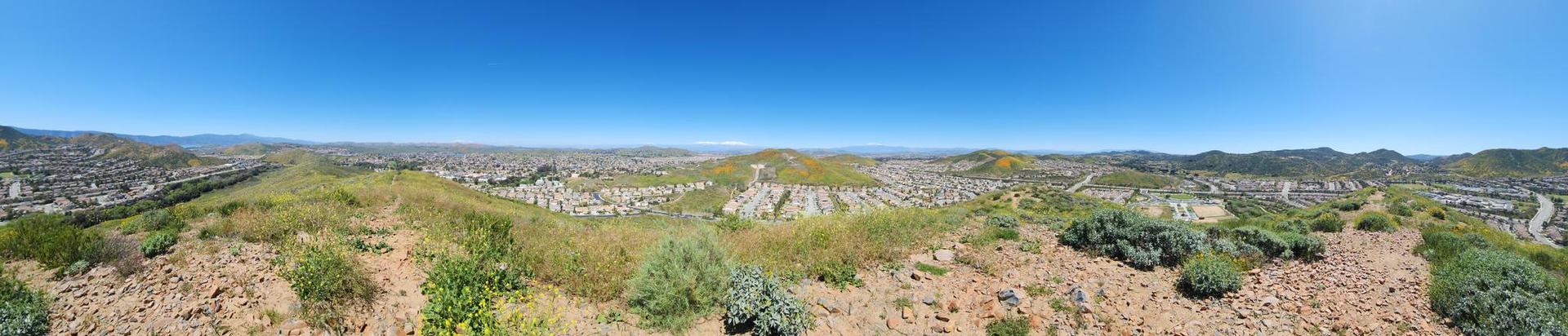 Panoramic view of rolling hills with sparse vegetation and distant urban areas.