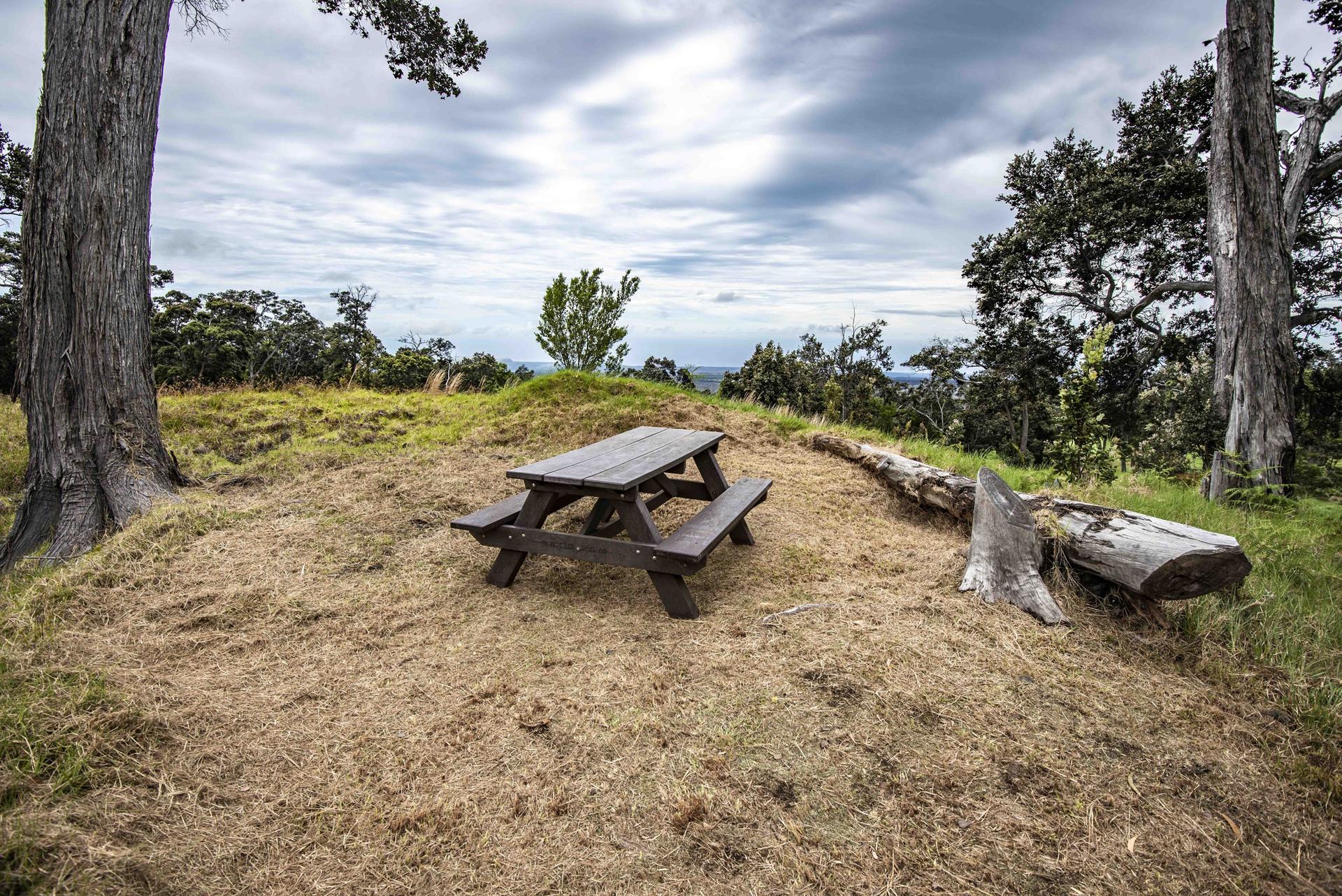 A wooden picnic table on a grassy hill under a cloudy sky.