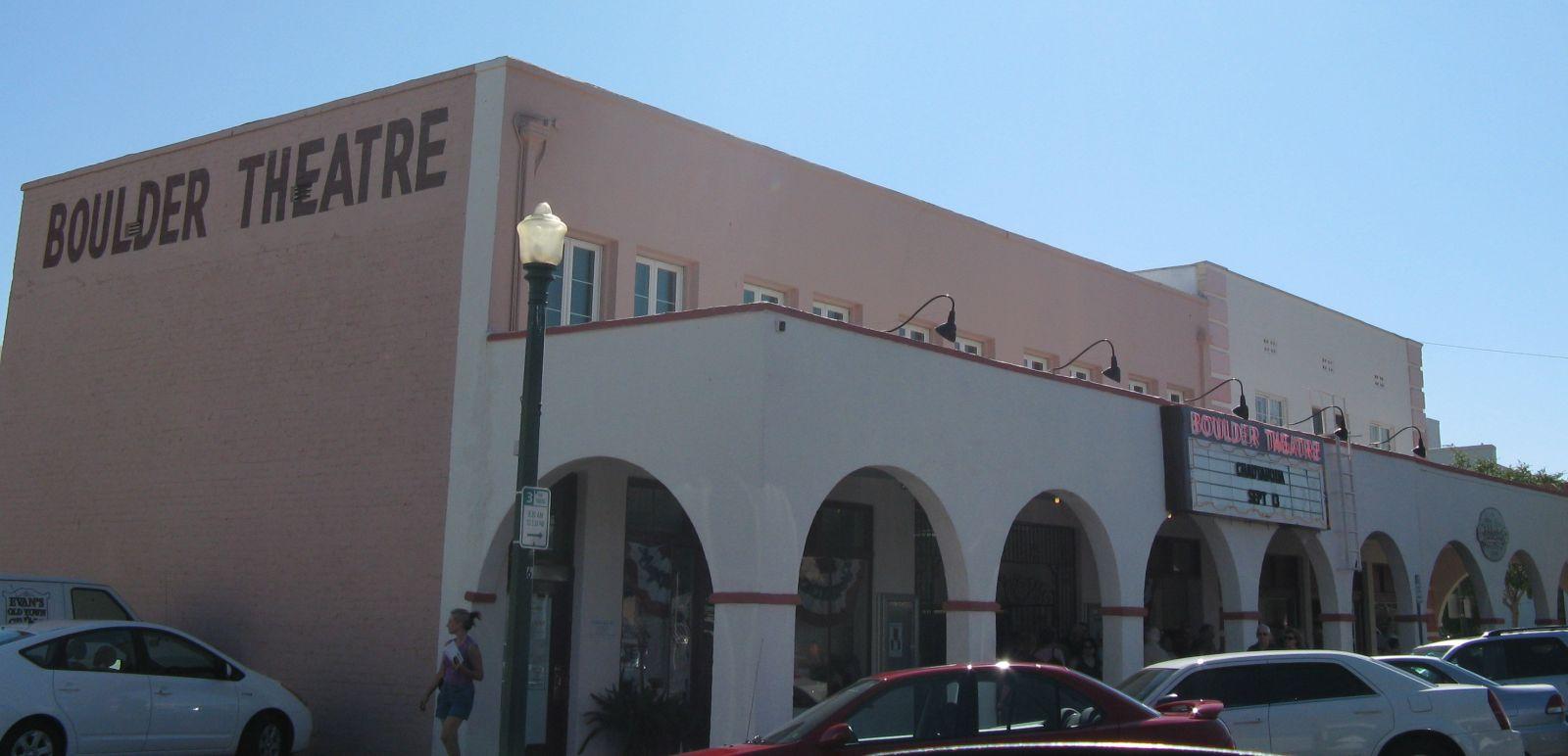 Pink and white building with 'THEATRE' sign, cars parked in front.