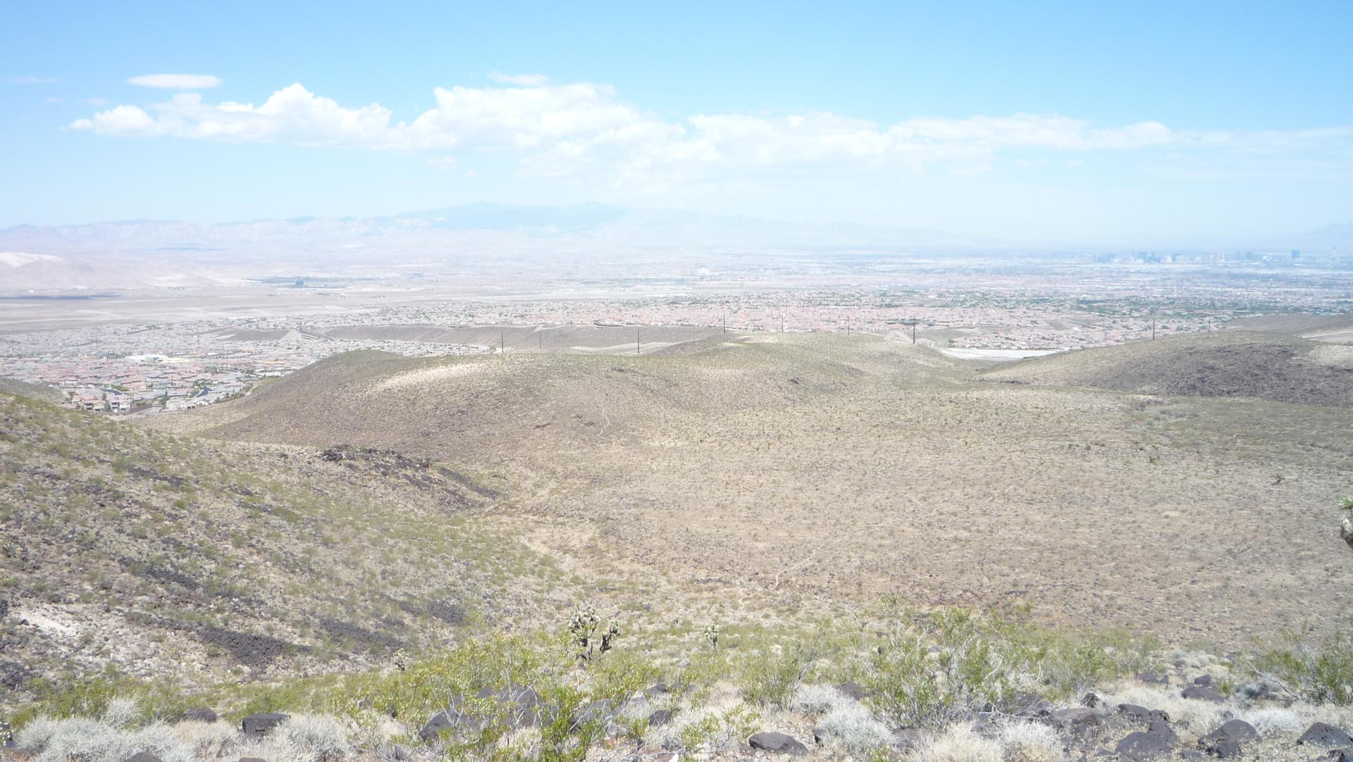 Expansive arid landscape with rolling hills and a distant city under a bright sky.