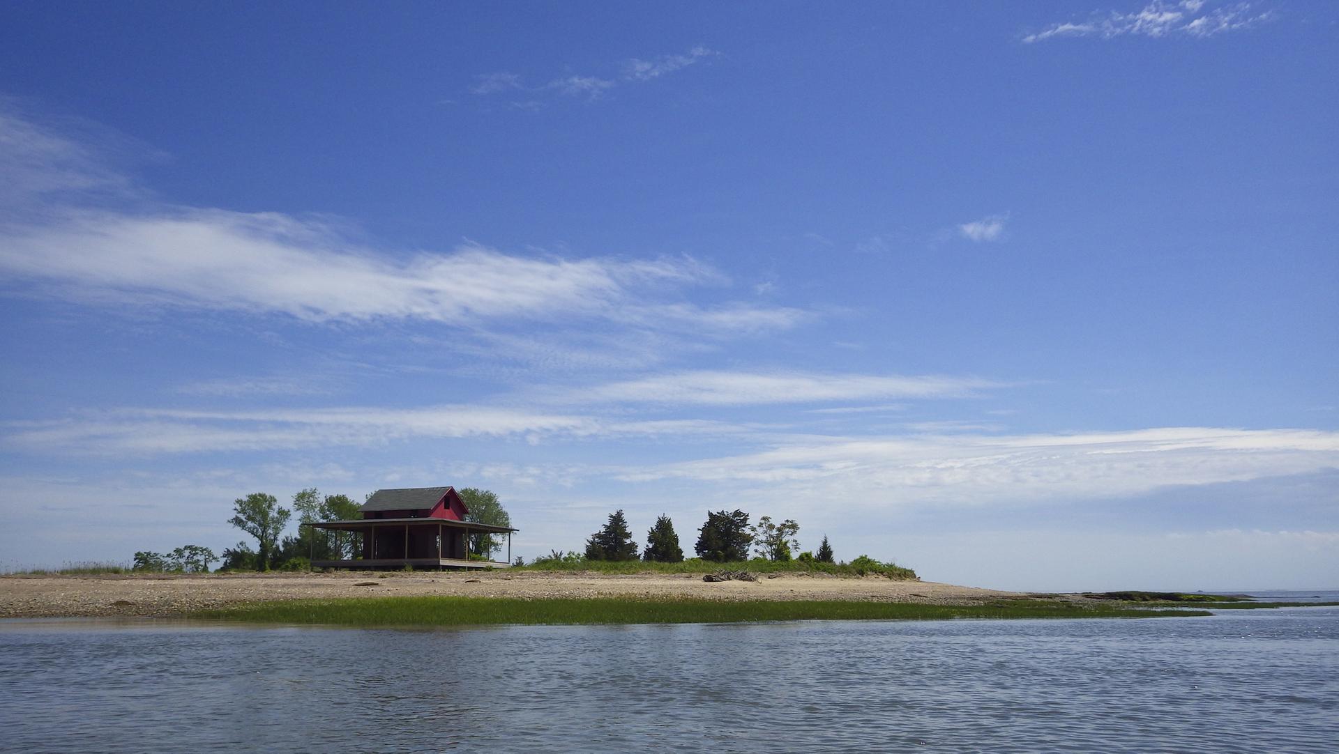 A small red house on a sandy island under a bright blue sky.