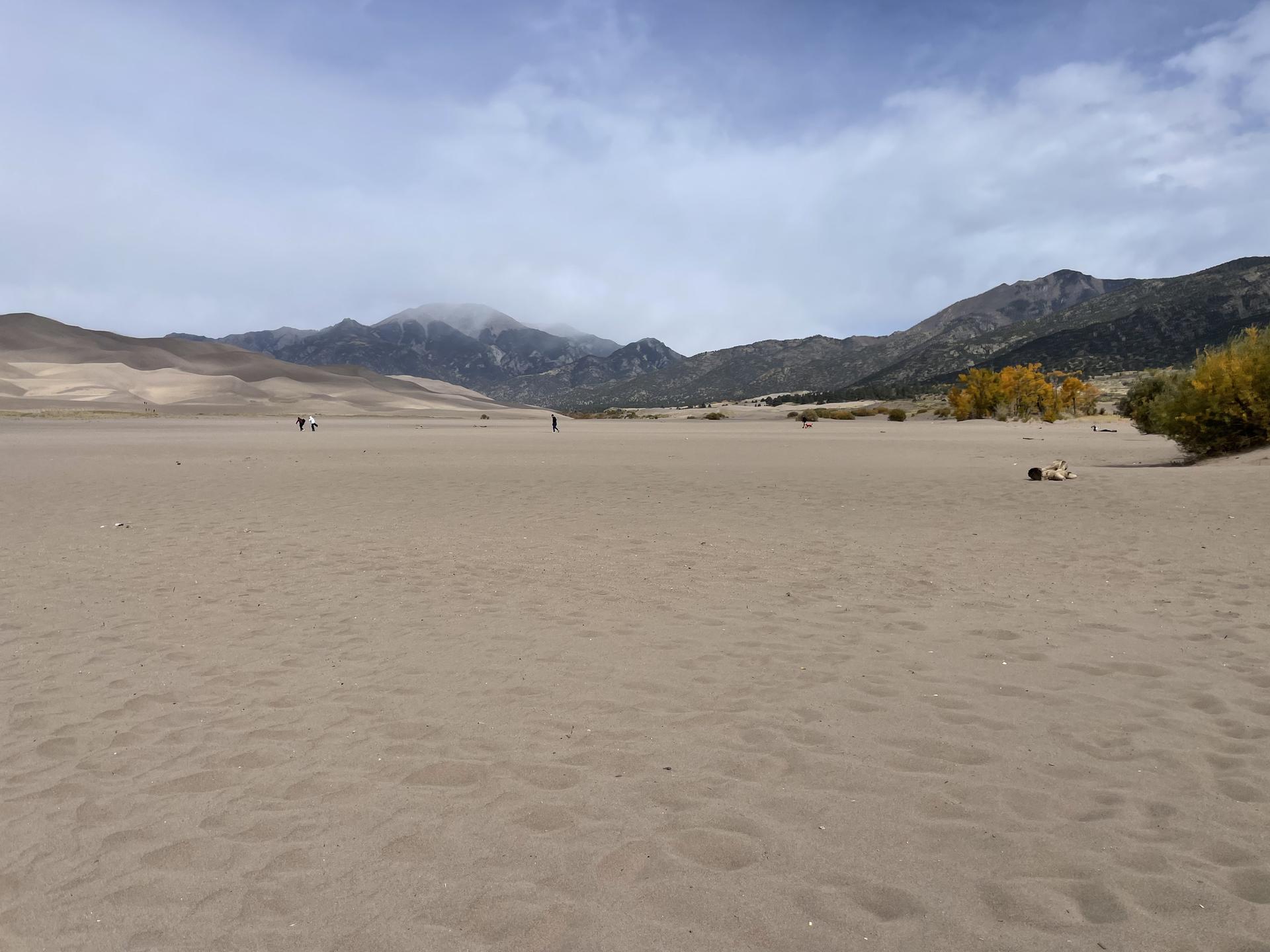 A wide, flat sandy expanse with distant mountains and small figures walking.