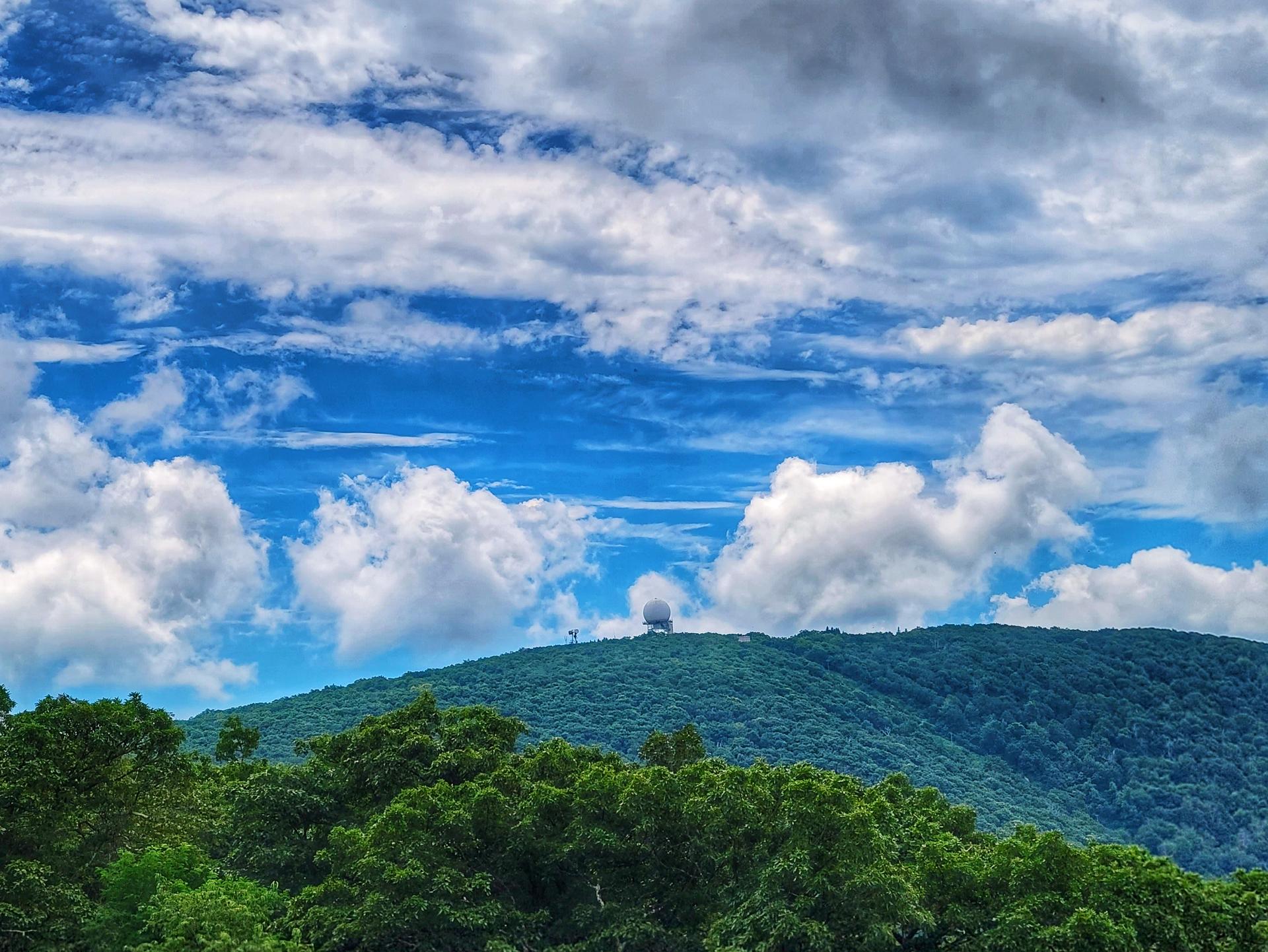 Distant dome building on a lush green mountain under a bright, cloudy sky.