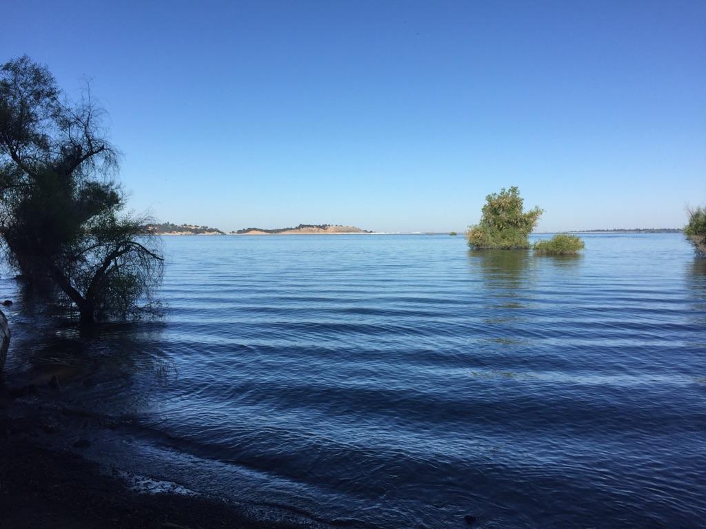 Wide blue lake under clear sky with small tree-covered islands.