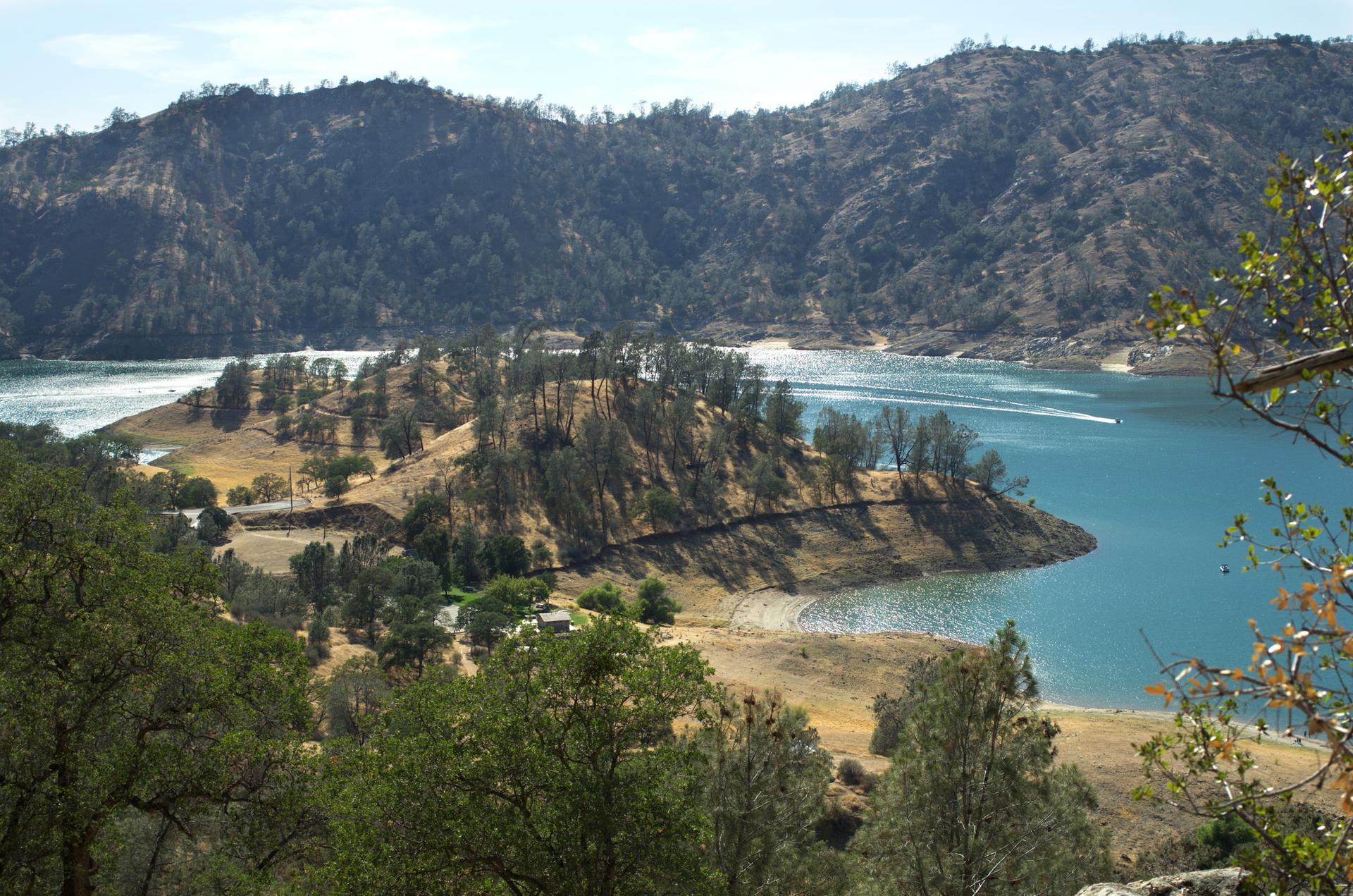 Expansive blue lake surrounded by forested hills under bright daylight.