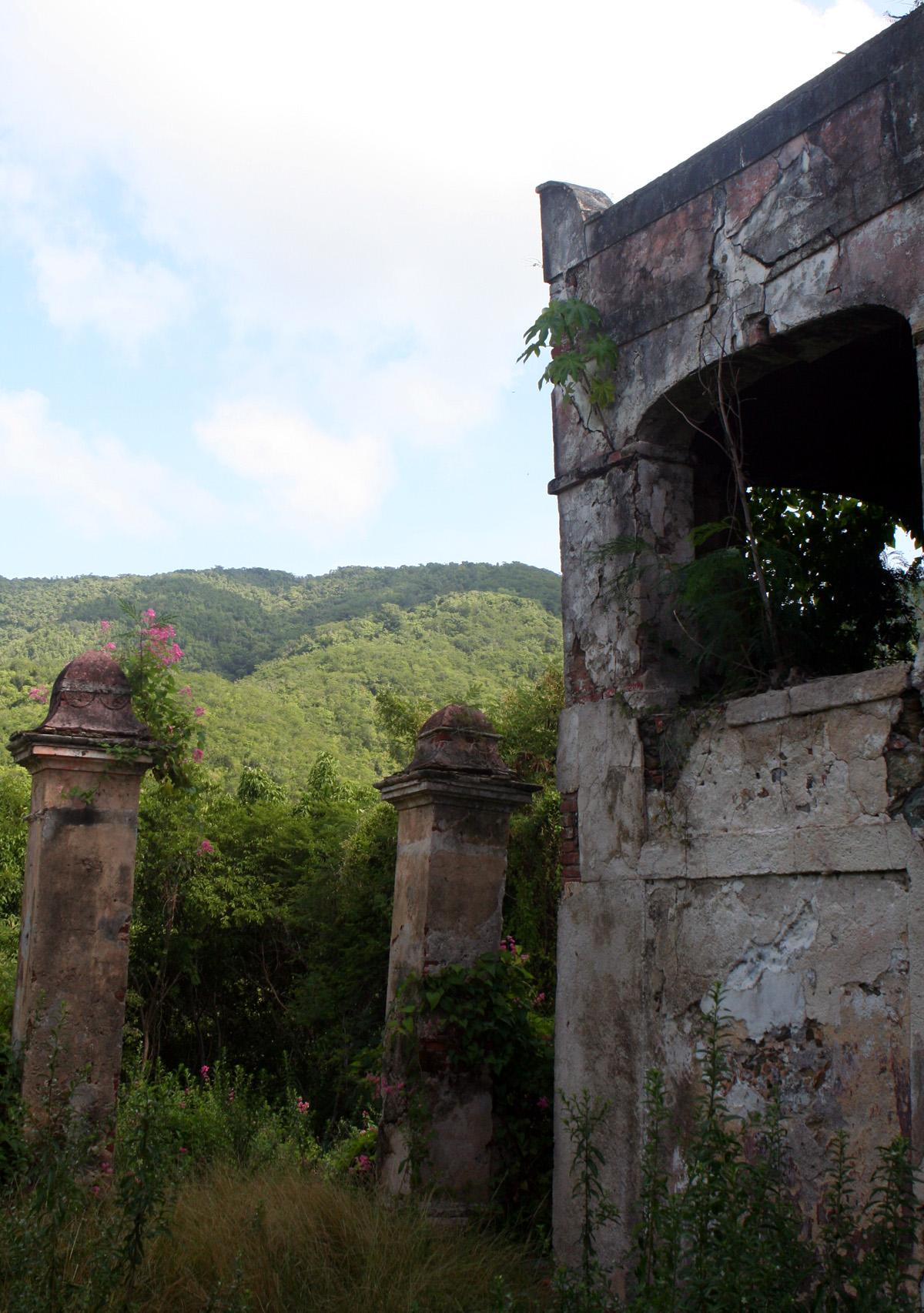 Overgrown stone ruins with archways and pillars against green hills.