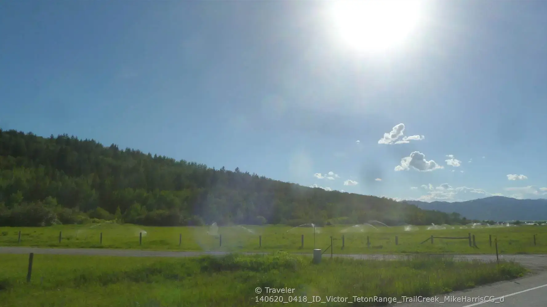 Bright sun shines over a green field and distant forested hills.