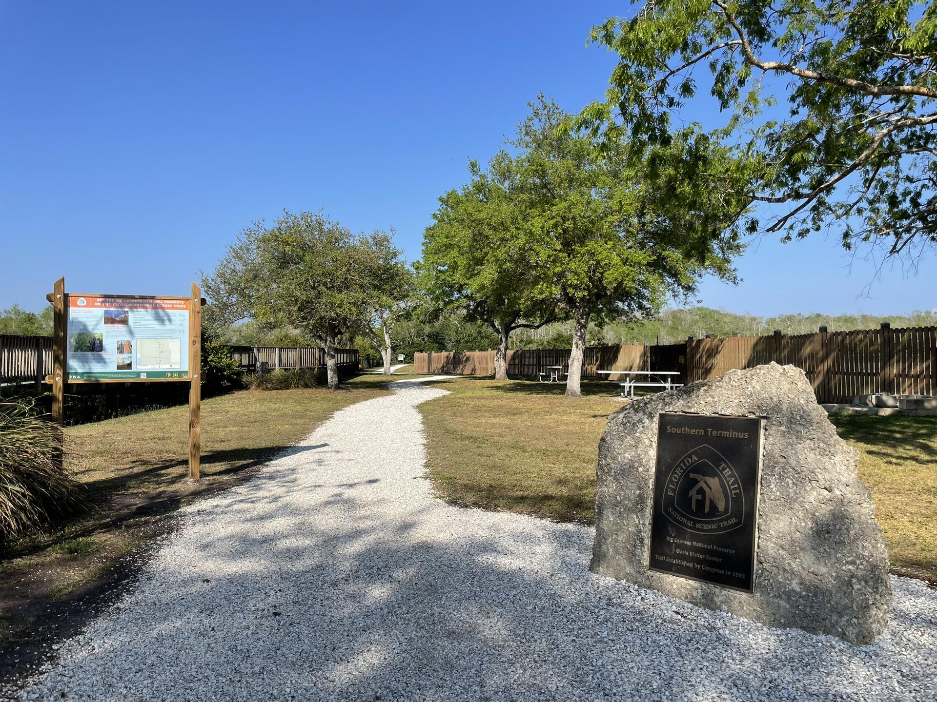 Gravel path leading to a picnic area with signs under a clear sky.