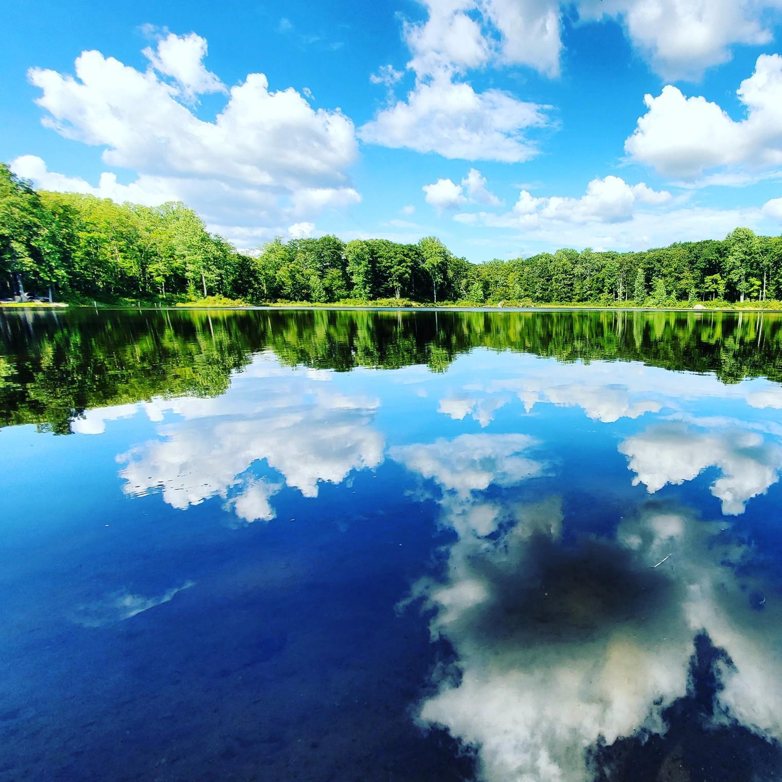A serene lake perfectly reflects a bright blue sky with white clouds.