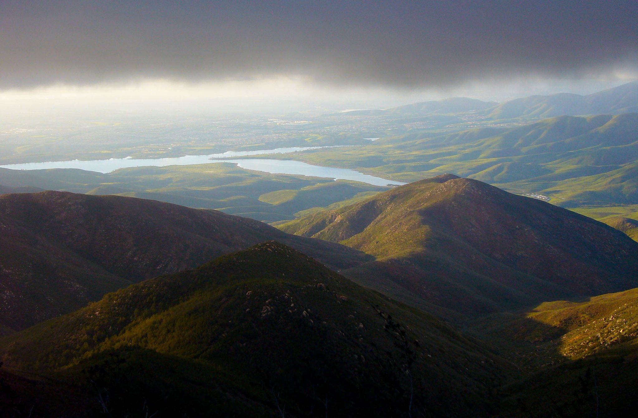 Dramatic view of green mountains, a distant lake, and stormy skies. - Otay Mountain via Minnewawa Truck Trail